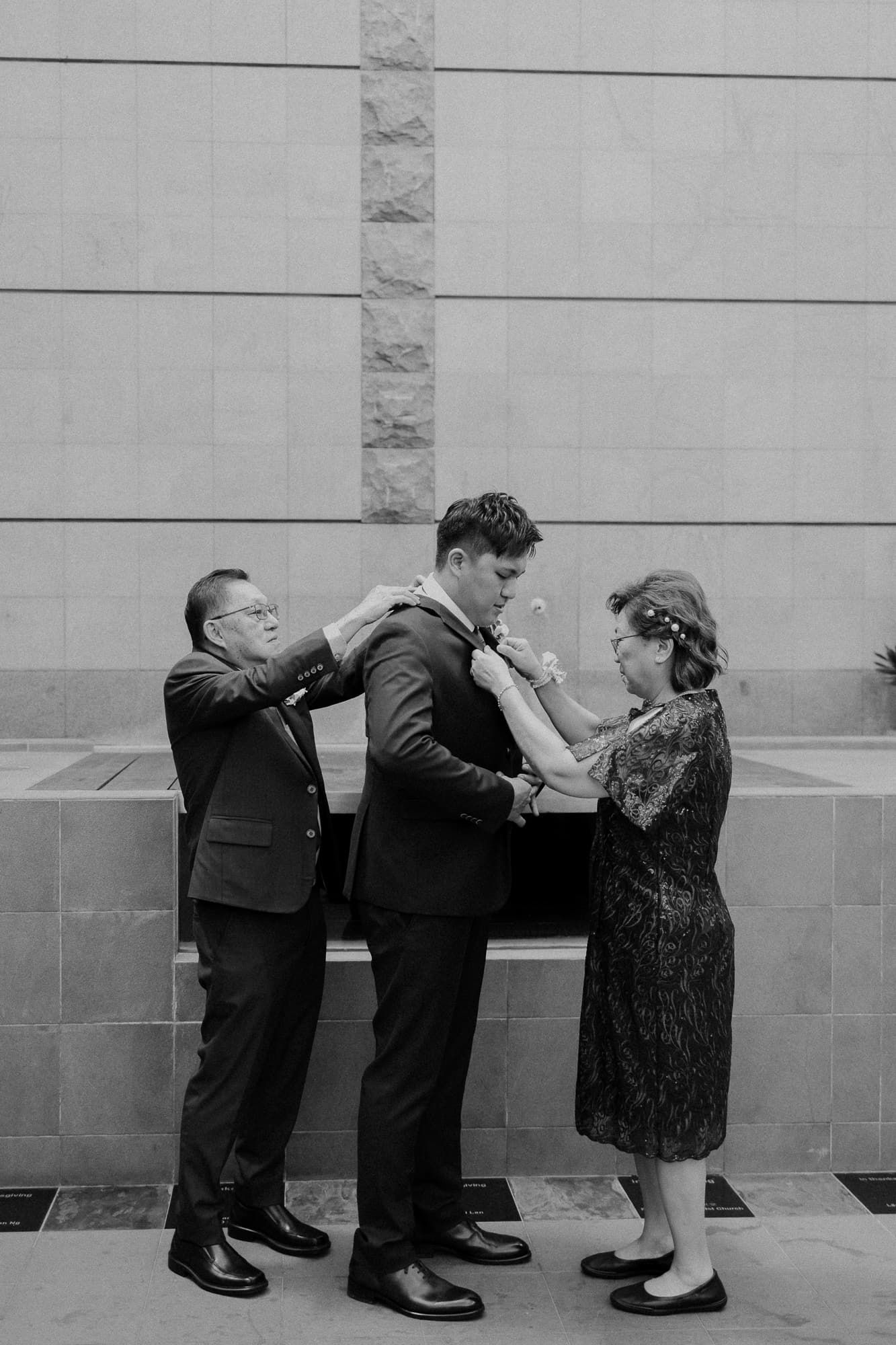 Black and white photo of family members adjusting formal attire before ceremony.
