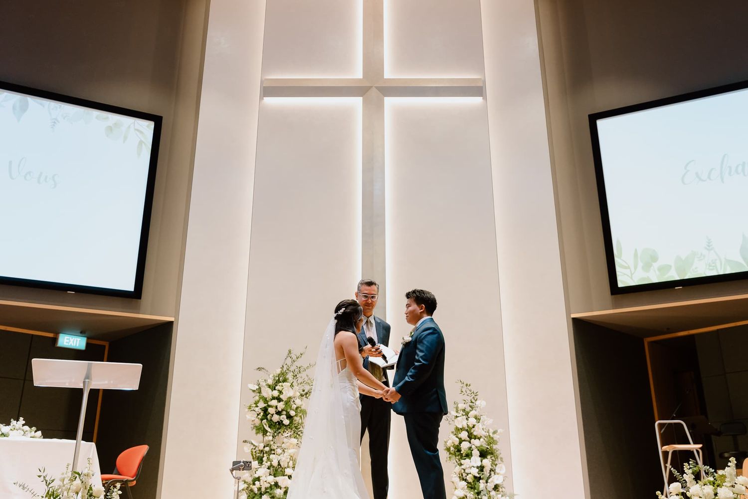 Modern church interior with white walls and cross visible during a wedding ceremony.