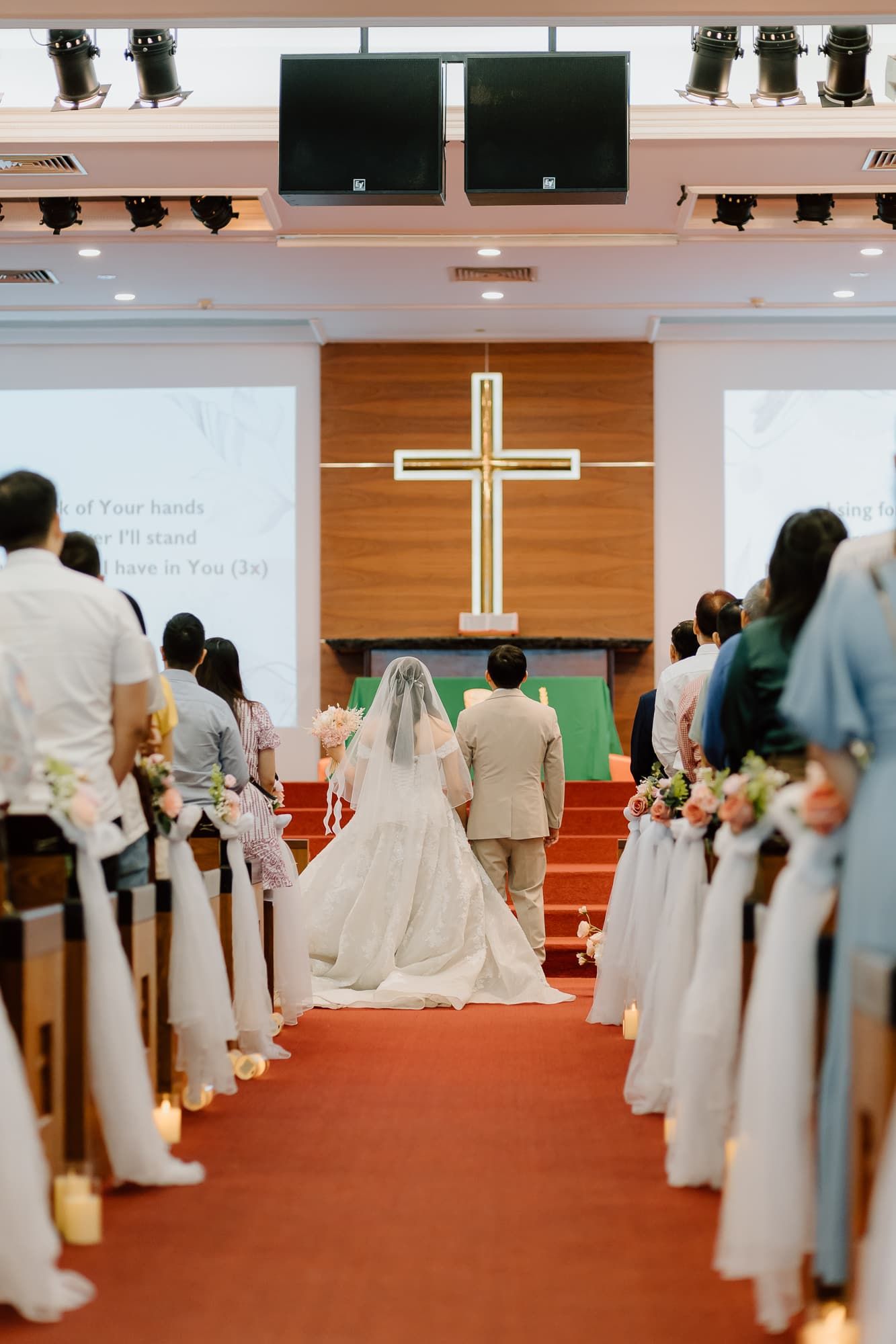 A church wedding ceremony with a illuminated cross on wooden wall and decorated aisle.