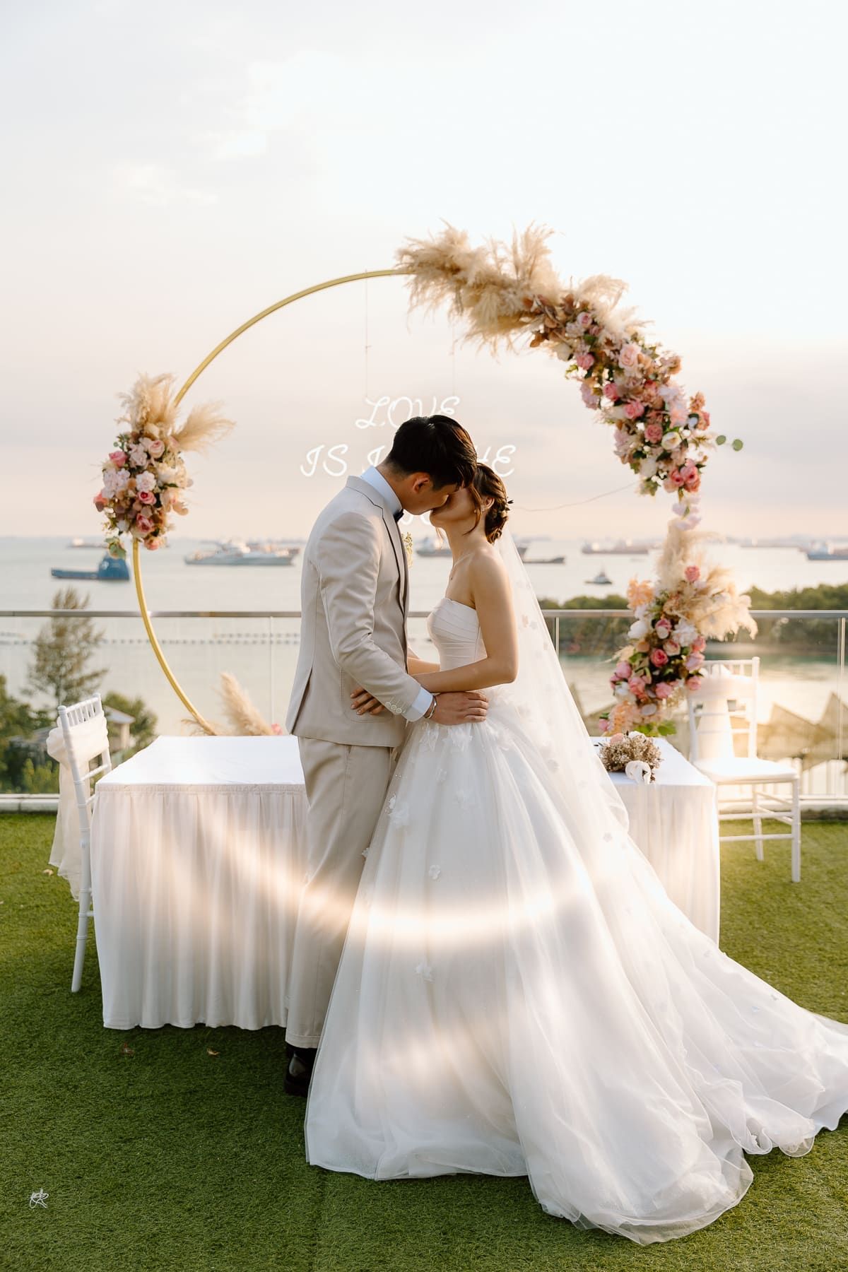 Romantic portrait of newlyweds embracing under a floral arch during golden hour.