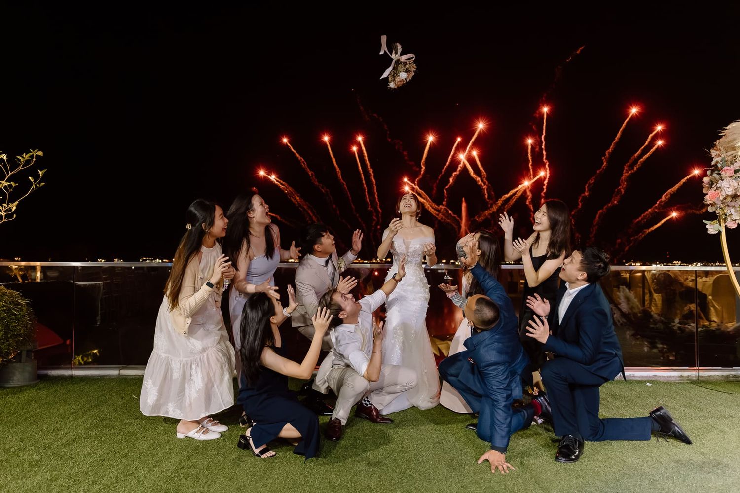 Wedding party posing for a fun group photo with fireworks in the background.