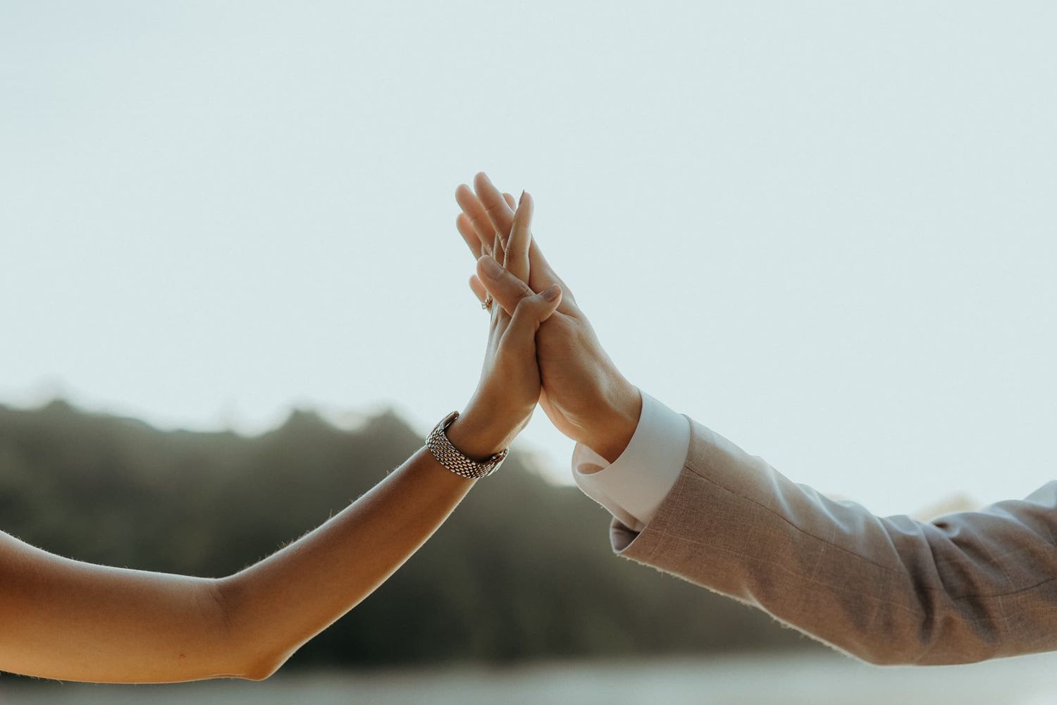 Silhouettes of hands reaching towards each other against a bright sky during golden hour.