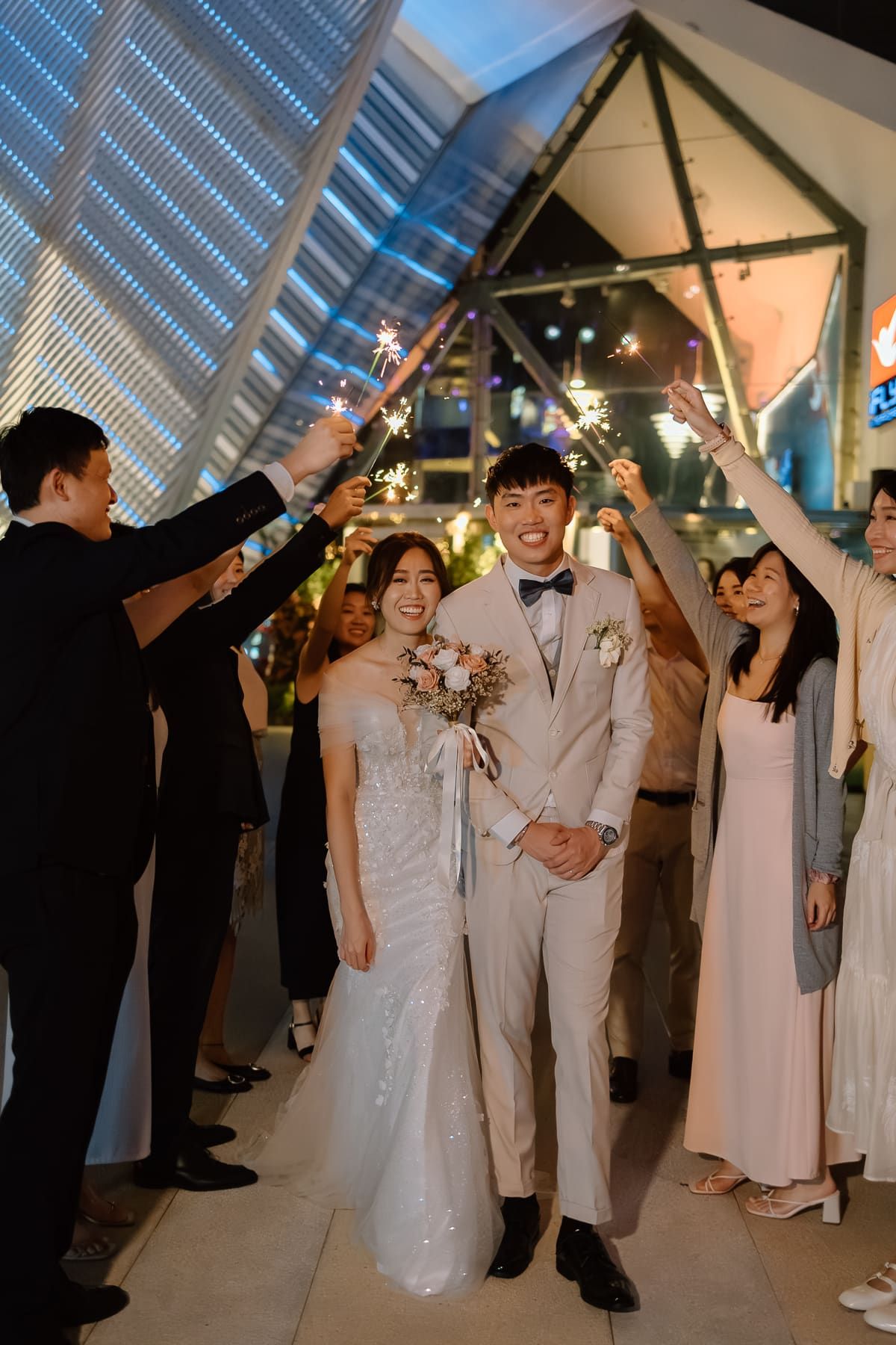 Wedding party walking under an illuminated geometric archway during celebration.