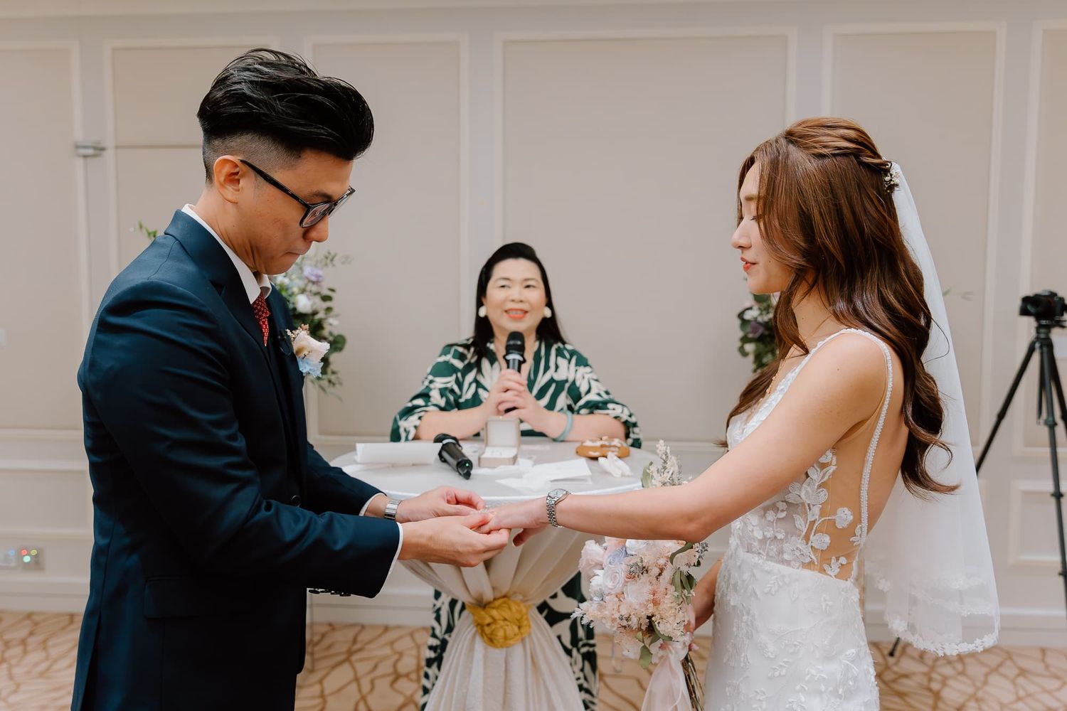 Romantic ring exchange ceremony during an indoor wedding with floral decorations.