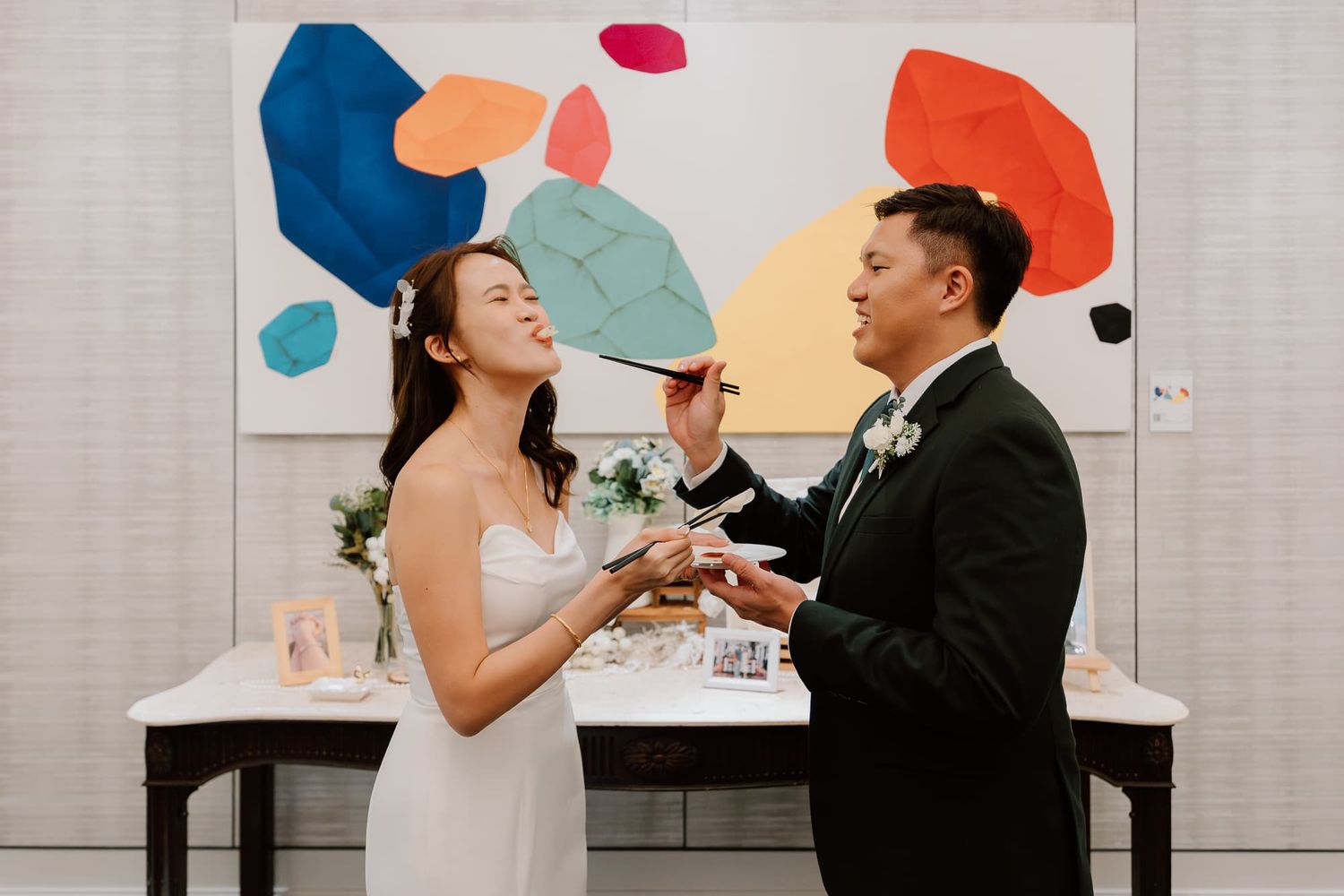 Colorful wedding cake cutting scene against vibrant abstract art background.
