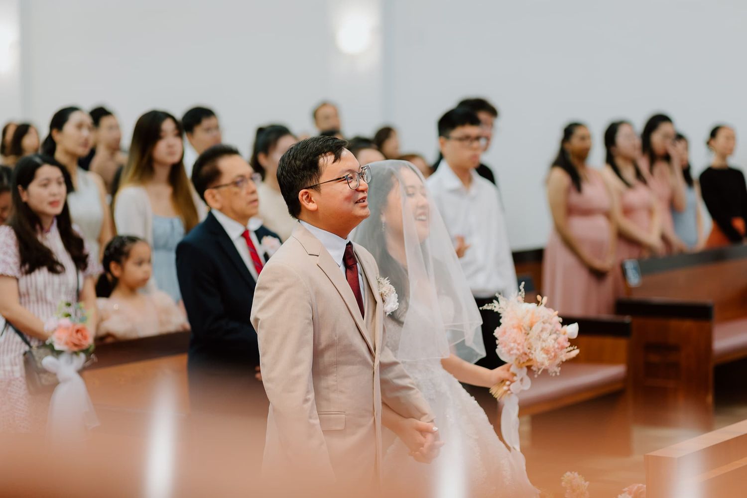 A couple stands at the altar during their church wedding ceremony surrounded by guests in formal attire.