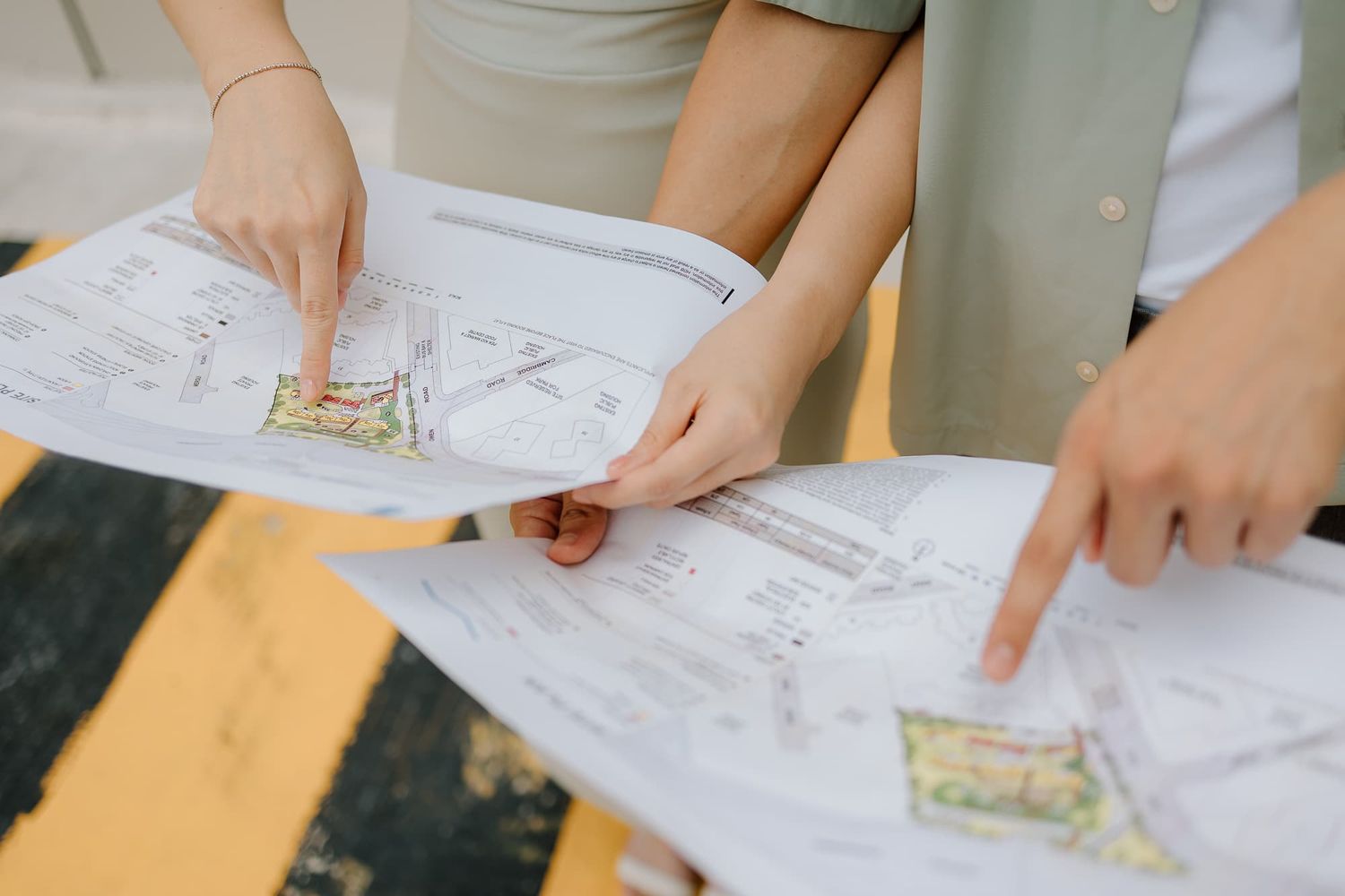 Hands pointing at architectural blueprints spread out on a wooden table.
