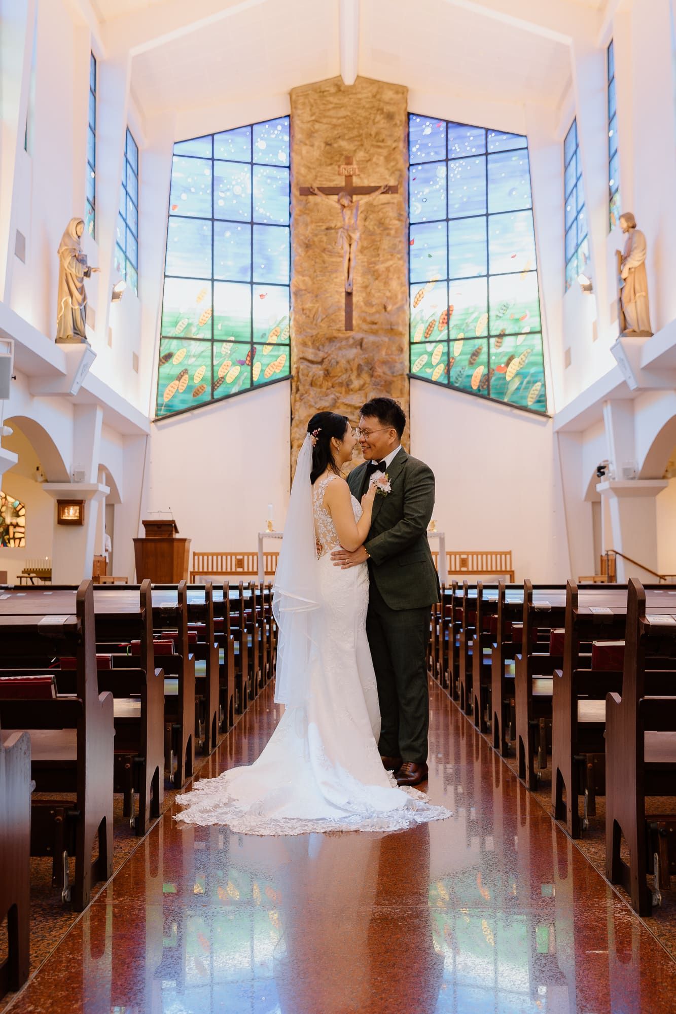 Bride and groom share an intimate moment in front of stained glass windows in a church sanctuary.