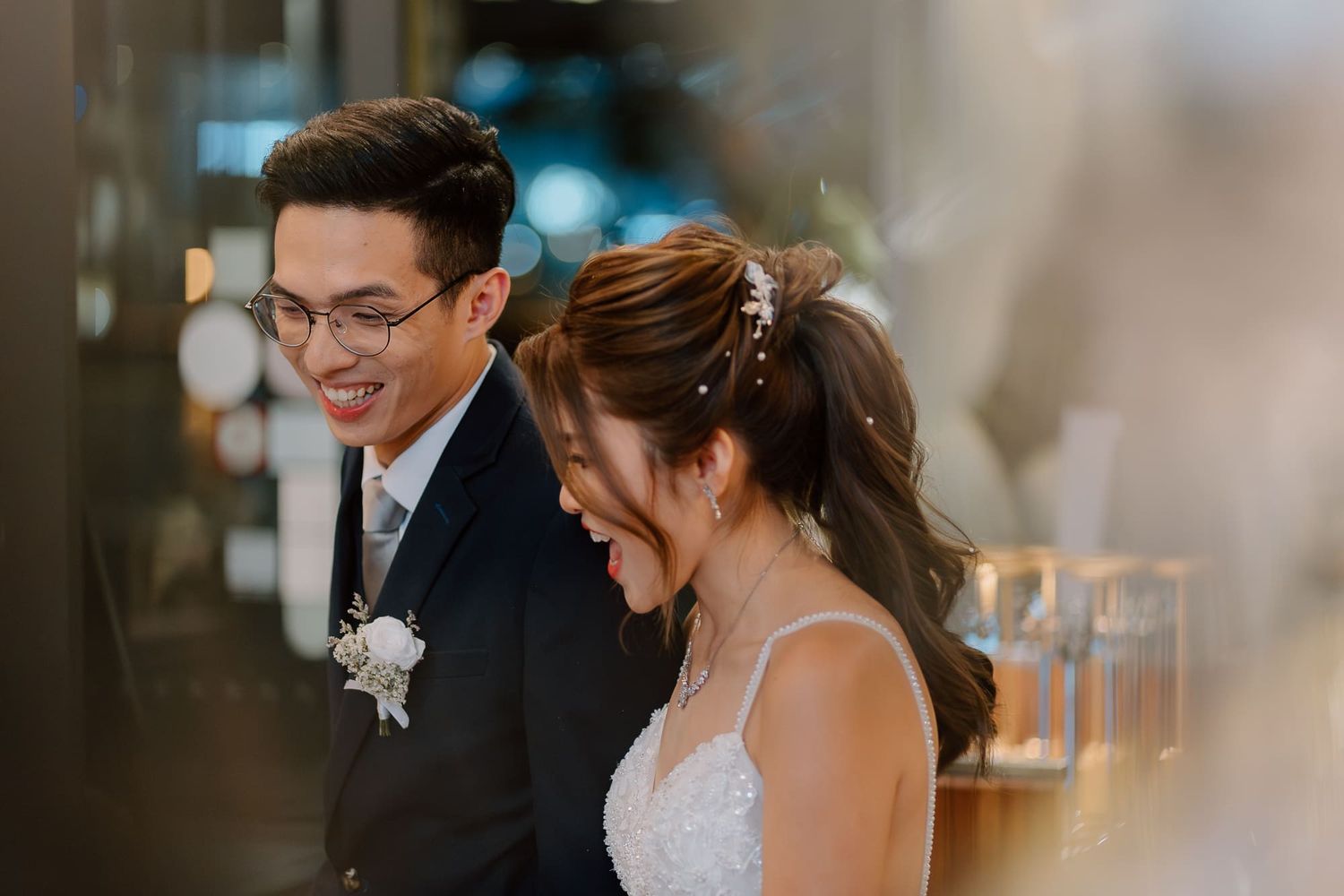 Joyful couple share a candid moment during their wedding celebration while wearing formal attire and smiling.