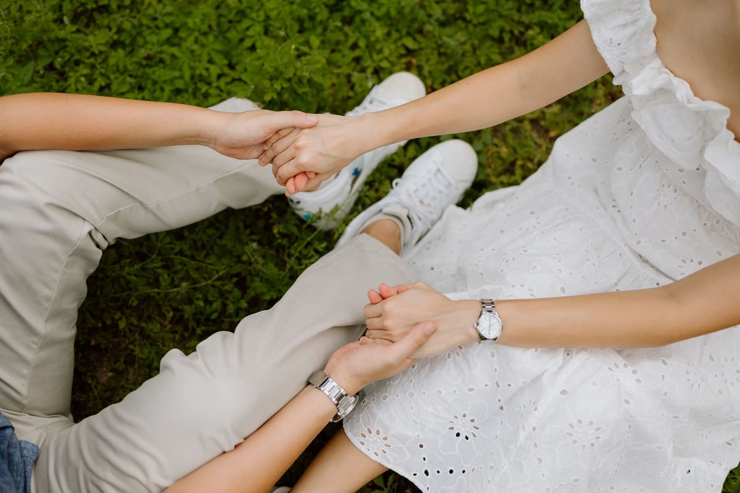 Close up of hands touching while sitting on grass outdoors.