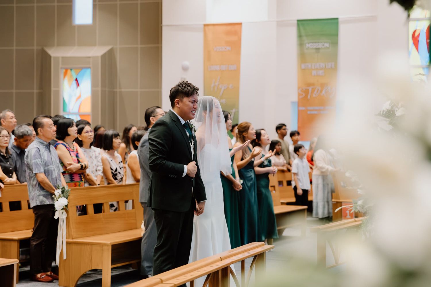Newlyweds stand together in church with decorated pews and banner displays.