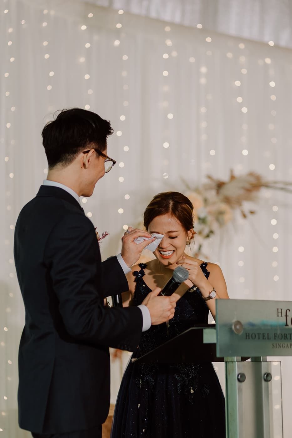 Couple sharing a playful moment in front of a twinkle light backdrop at their wedding reception.
