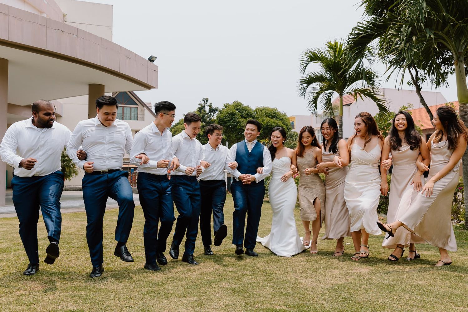 Wedding party members sitting in a line on grass for fun group photo.