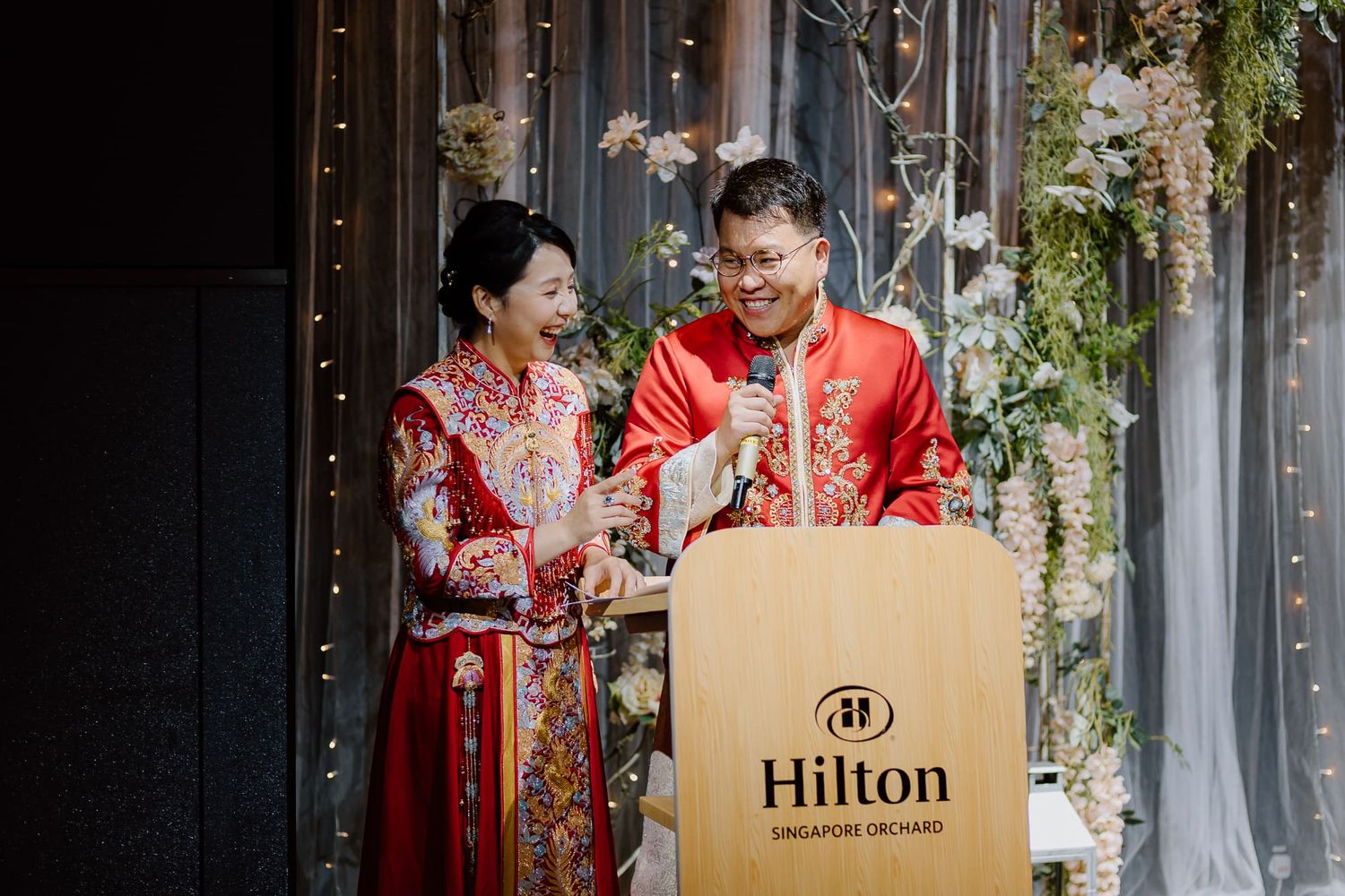 People in traditional red attire carrying shopping bags from luxury brands and laughing together on a street.