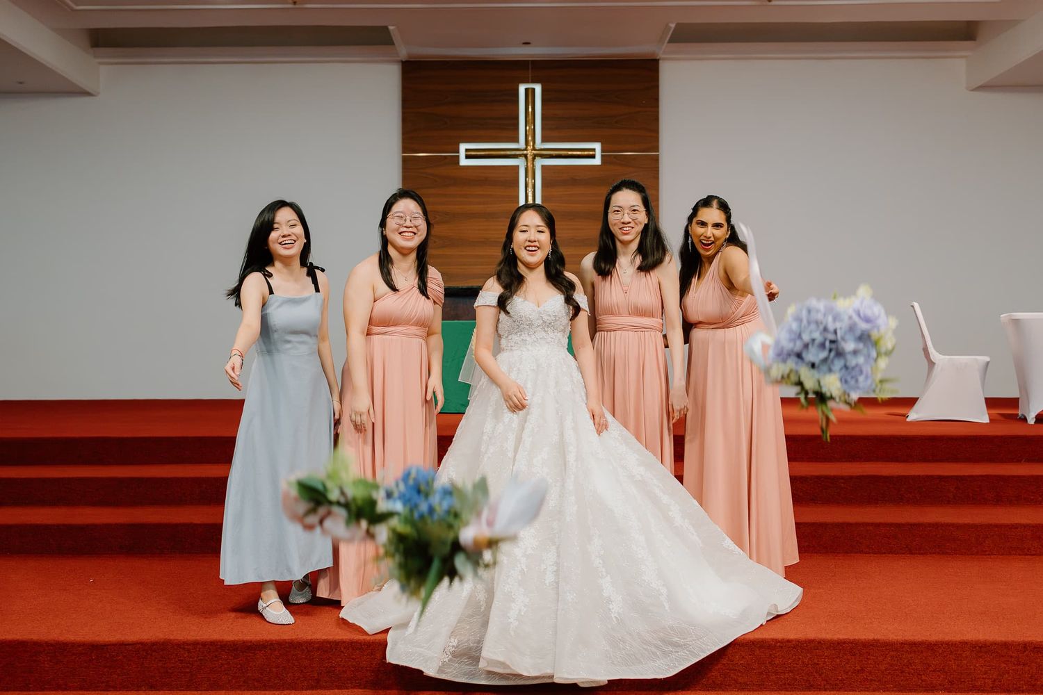 Wedding party featuring bridesmaids in pink and blue dresses posing with bride in white gown on church steps.