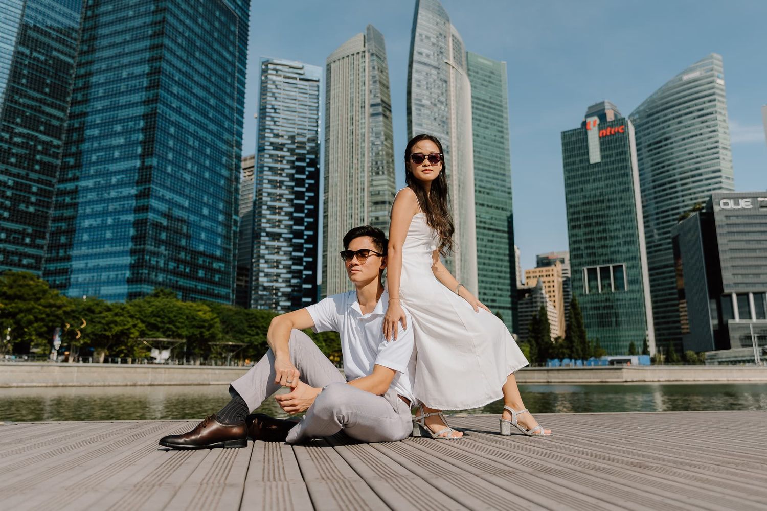 Stylish couple posing on wooden deck with modern urban skyline backdrop.