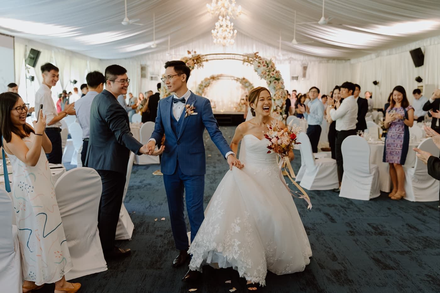 Wedding guests dance and celebrate in a large tented reception venue.