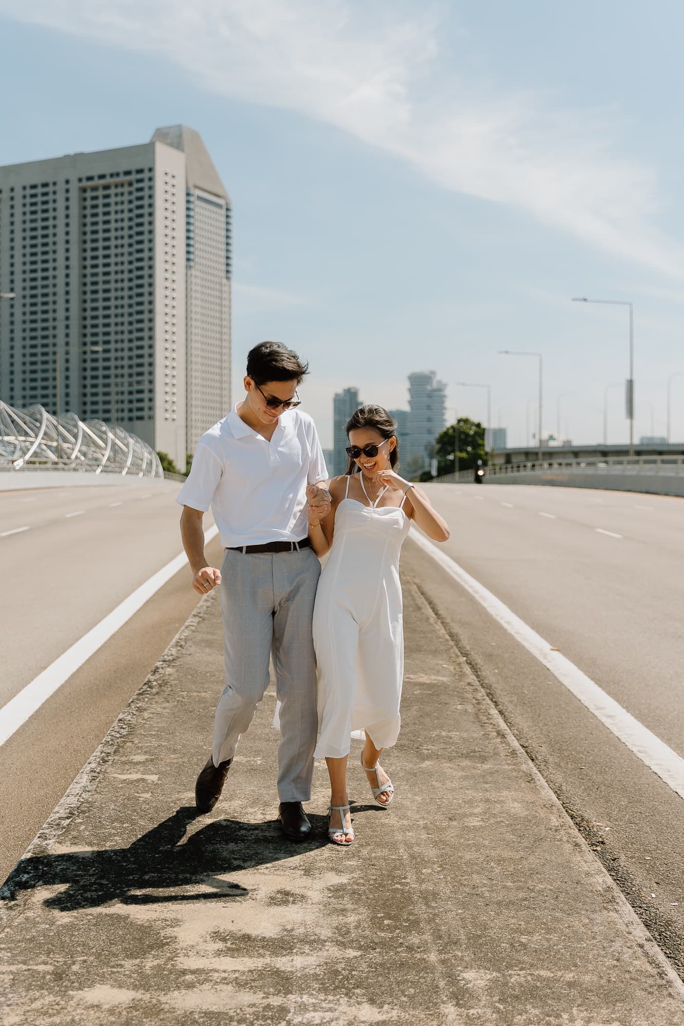 Couple in coordinated white outfits strolling along an urban pathway.