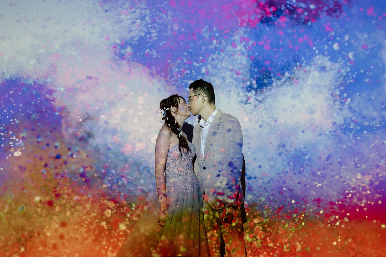 An artistic wedding portrait with colorful paint splash effects in purple and orange tones.