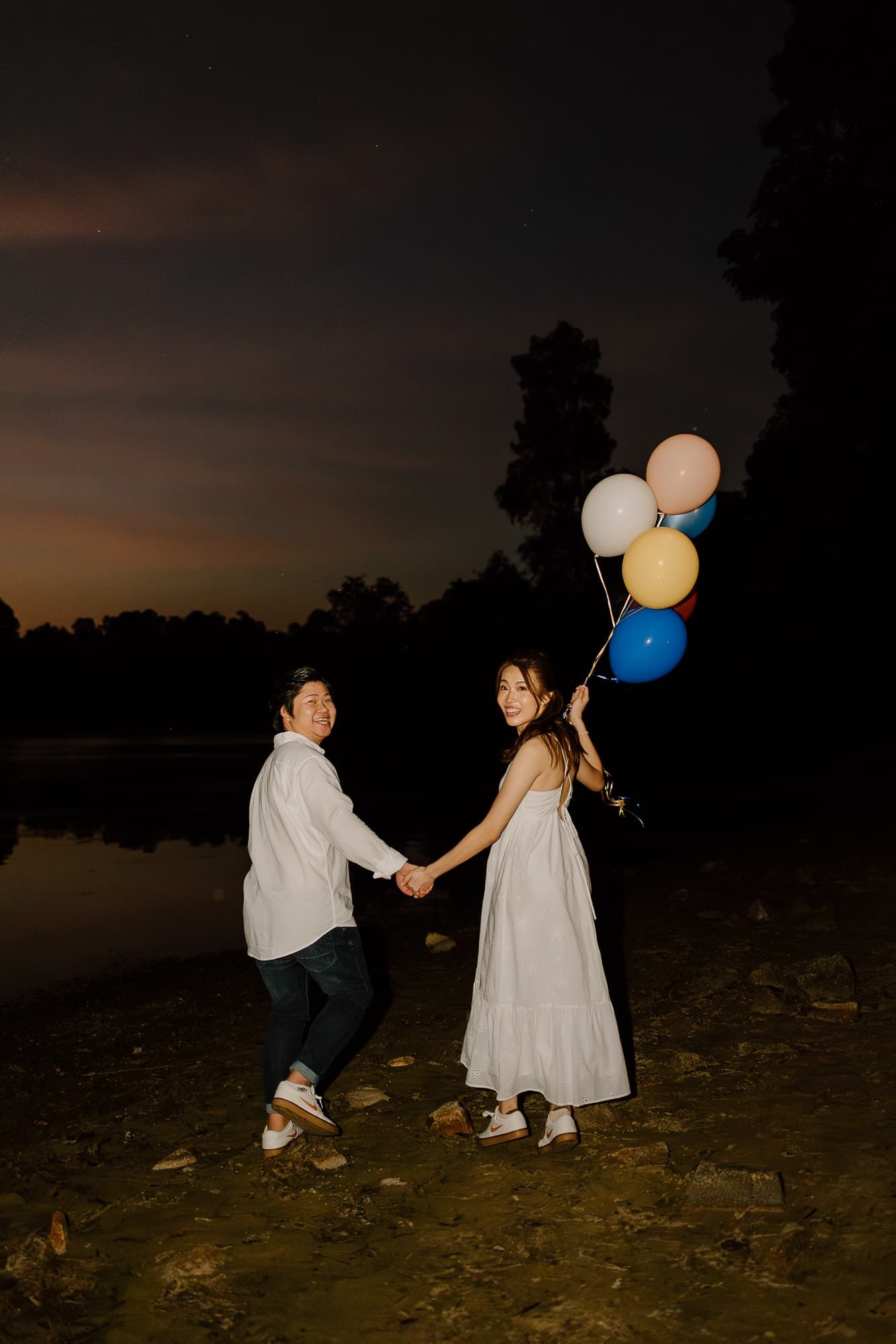 Two people playing with balloons on a beach at dusk.