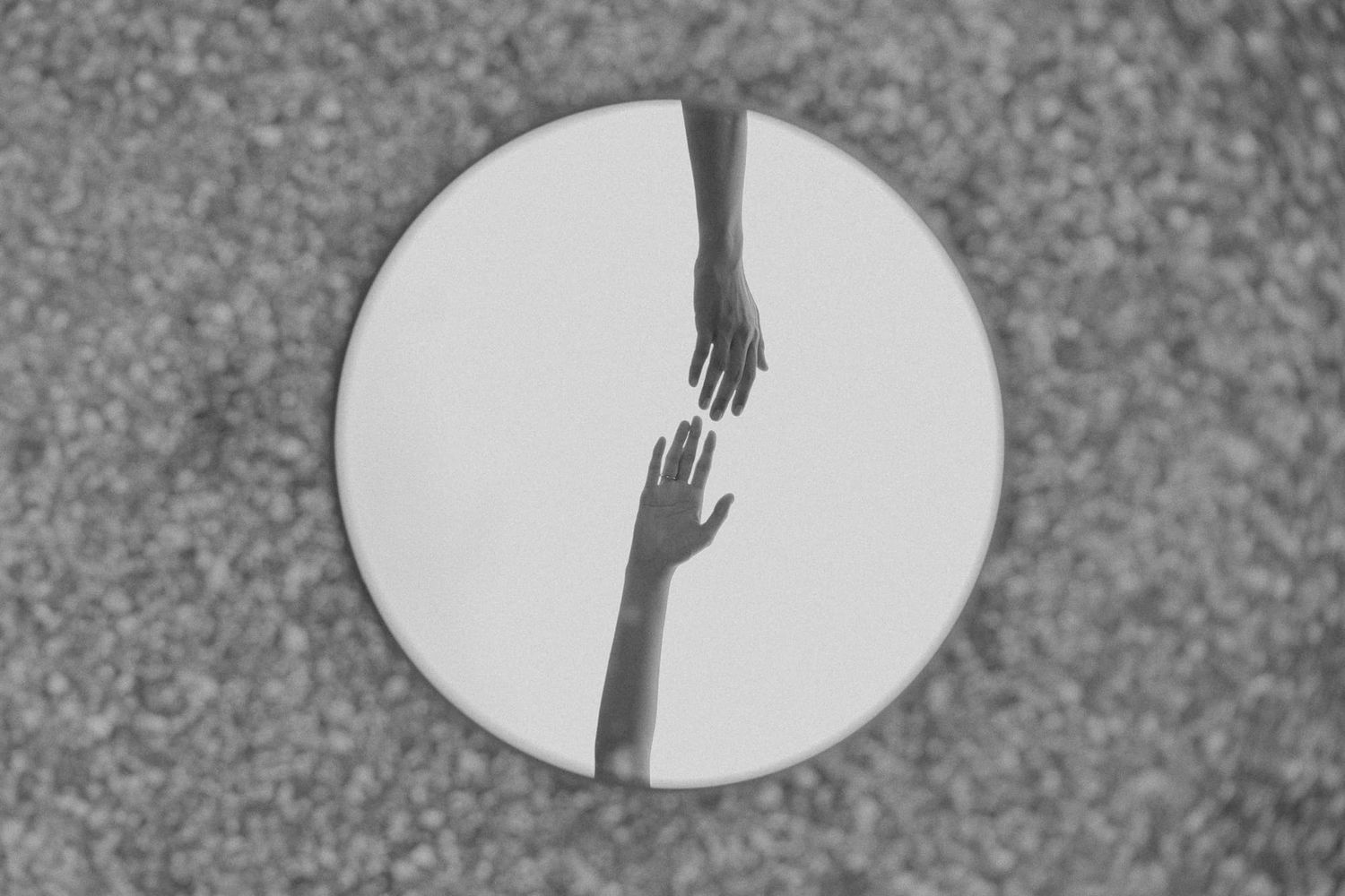 Black and white artistic photo of two hands reaching towards each other on a circular surface.