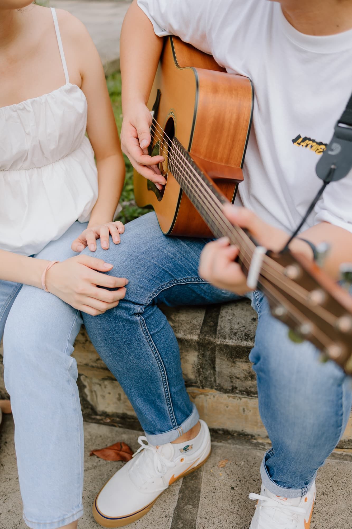 Close-up of hands on acoustic guitar strings as couple sits on stone steps.