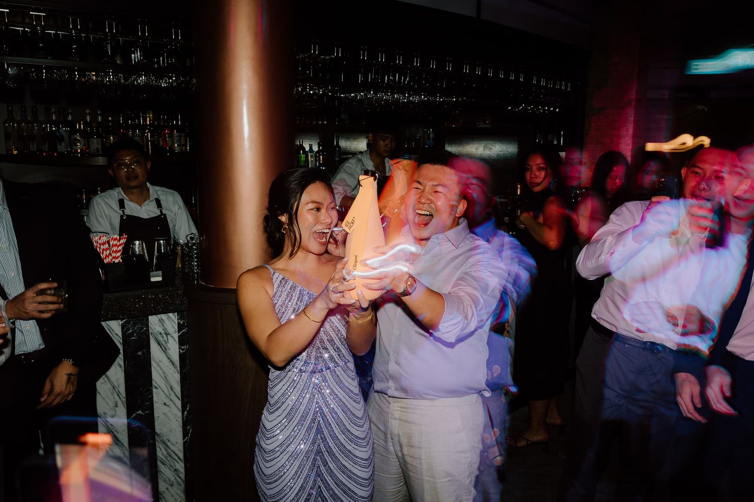 People dancing and celebrating at a dimly lit indoor venue with festive atmosphere.