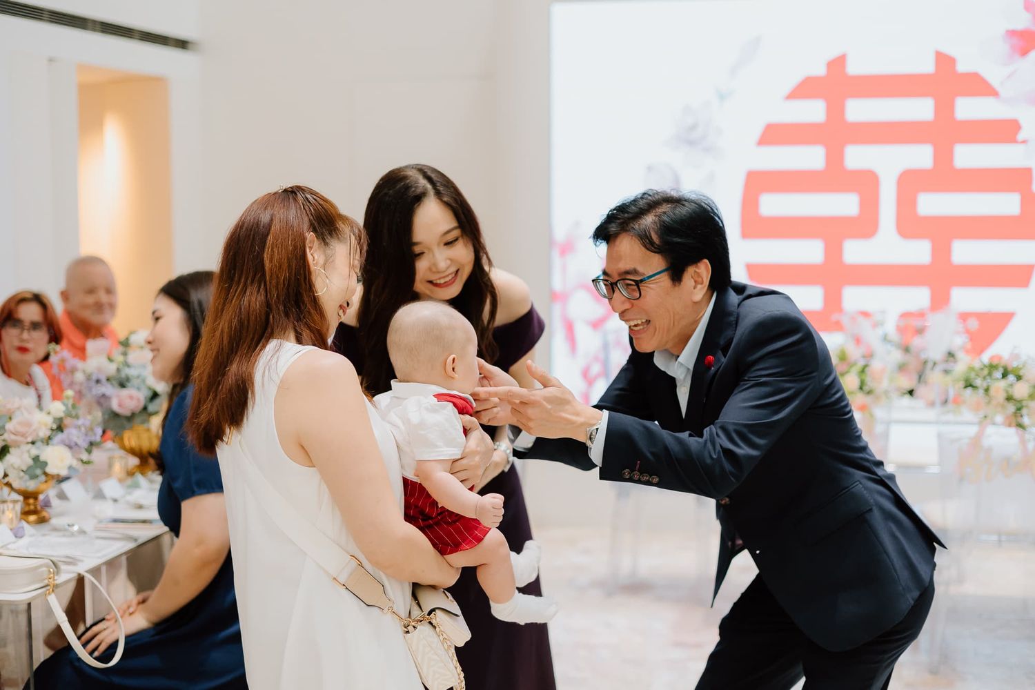 Wedding celebration with guests gathered around double happiness symbol backdrop.