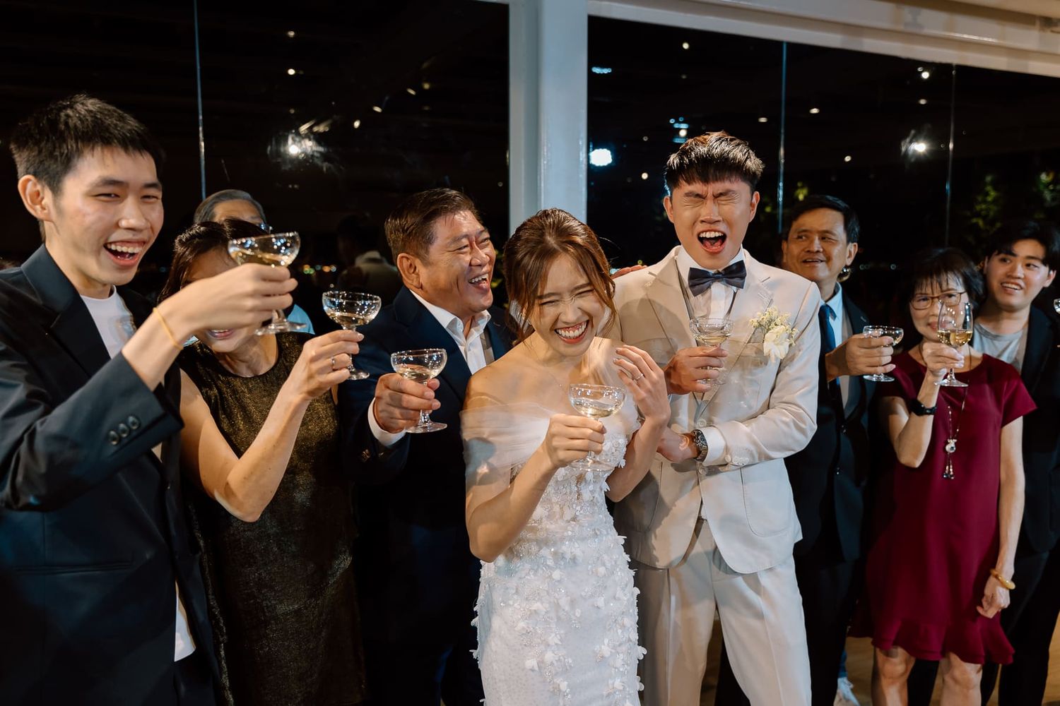 Wedding party and guests raise champagne glasses in celebration during an evening reception.