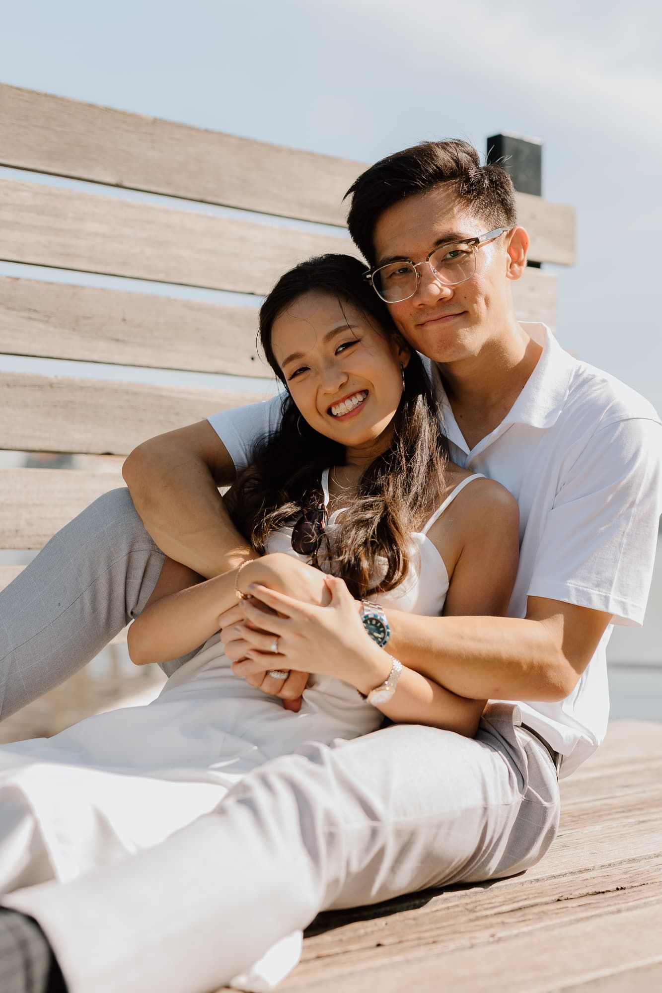 A couple shares an intimate moment while relaxing on wooden steps in casual white outfits.