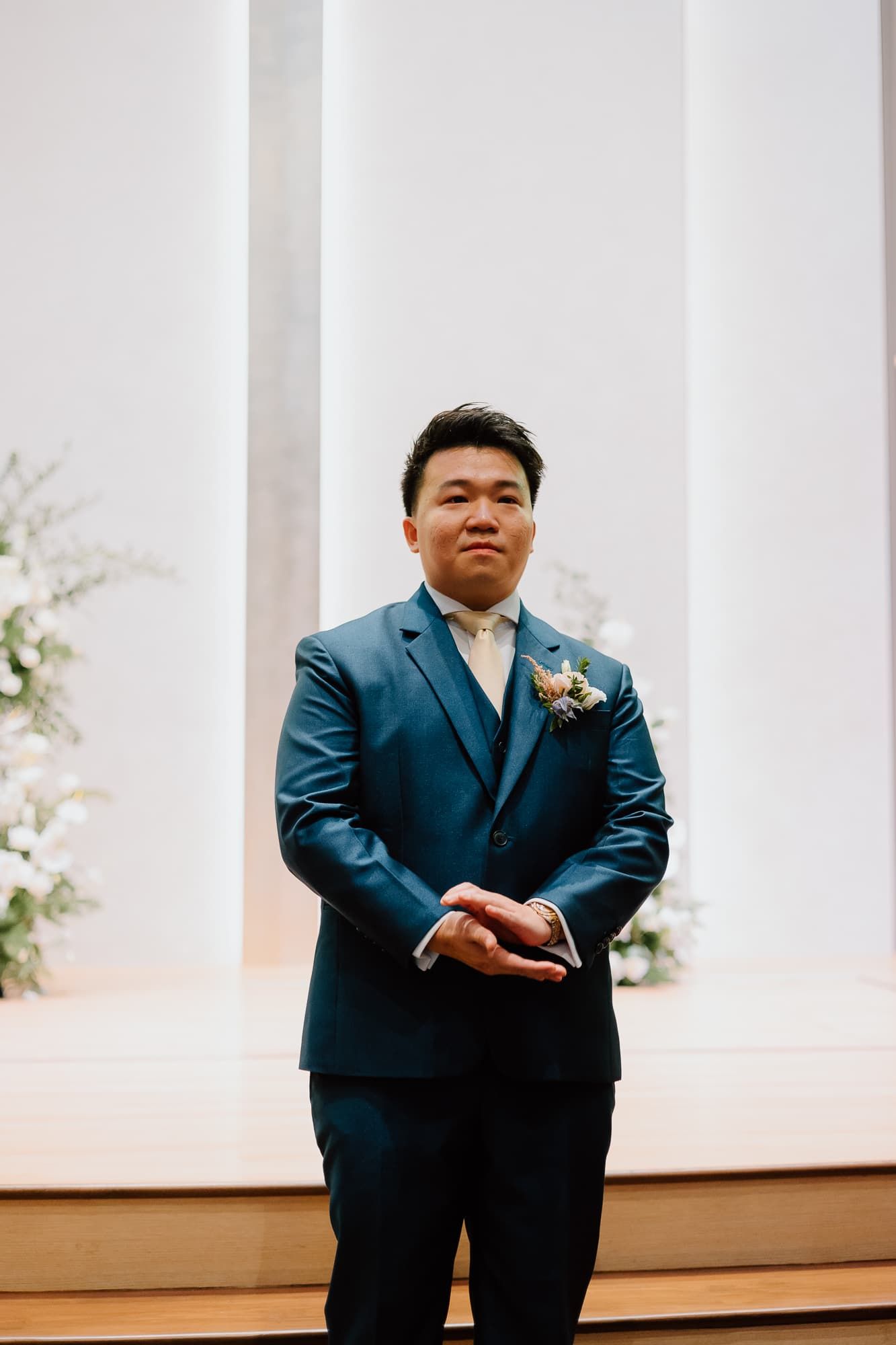 A person in a navy blue suit poses elegantly against a white backdrop during a wedding photoshoot.