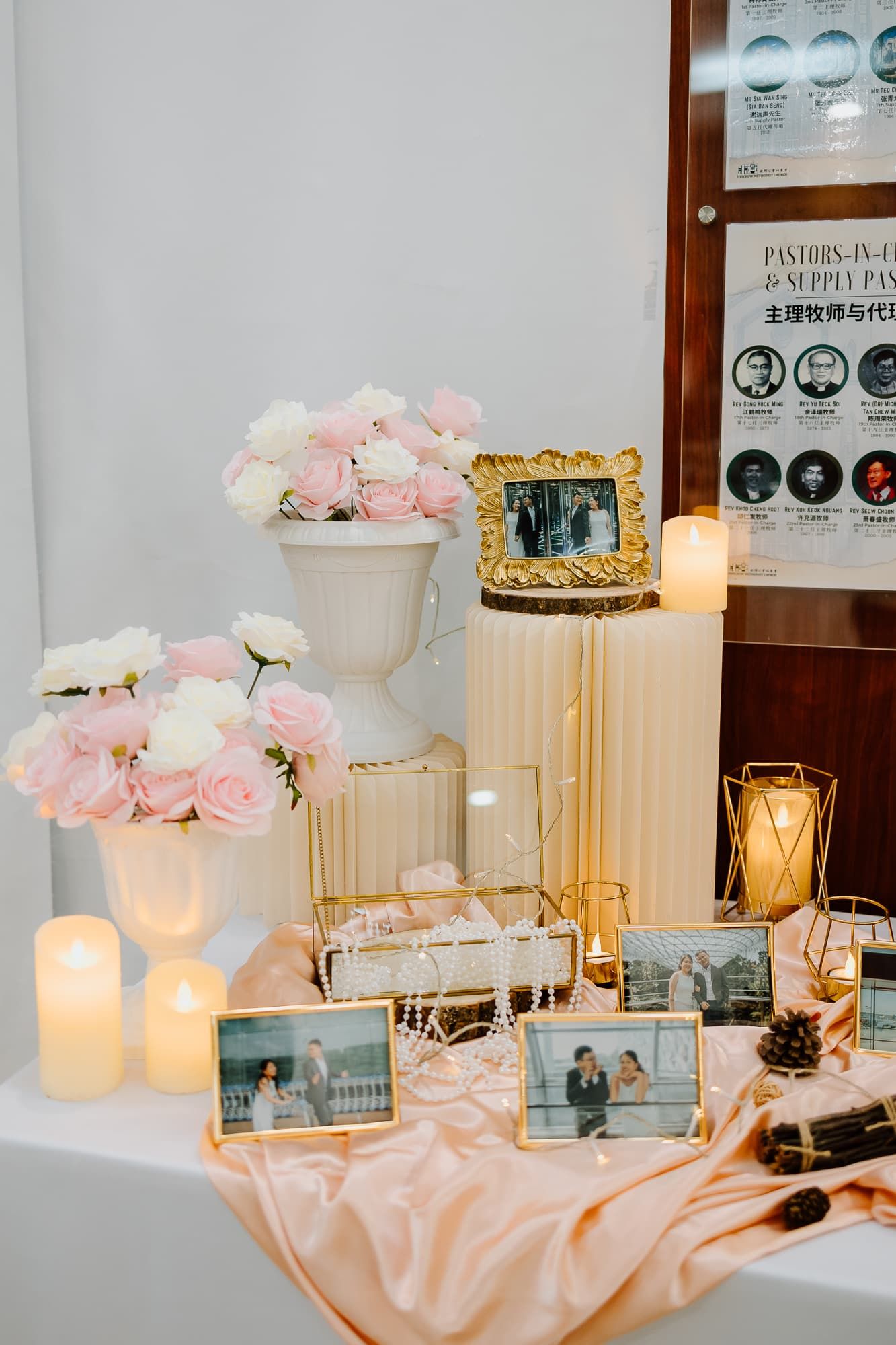 Elegant wedding reception display with pink roses, candles, and framed photos on silk fabric.