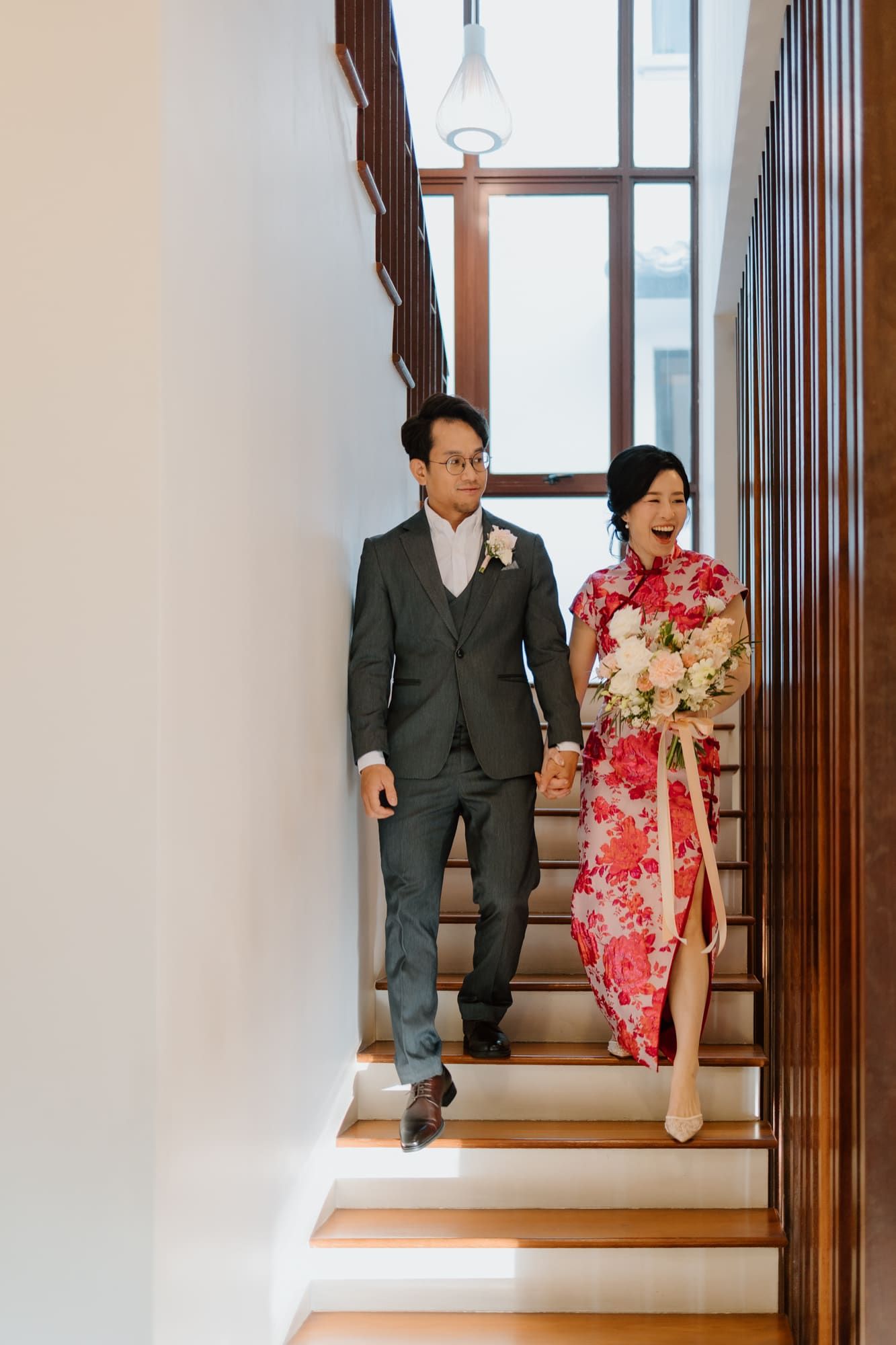 A couple in formal attire sits together on wooden stairs in an indoor setting.