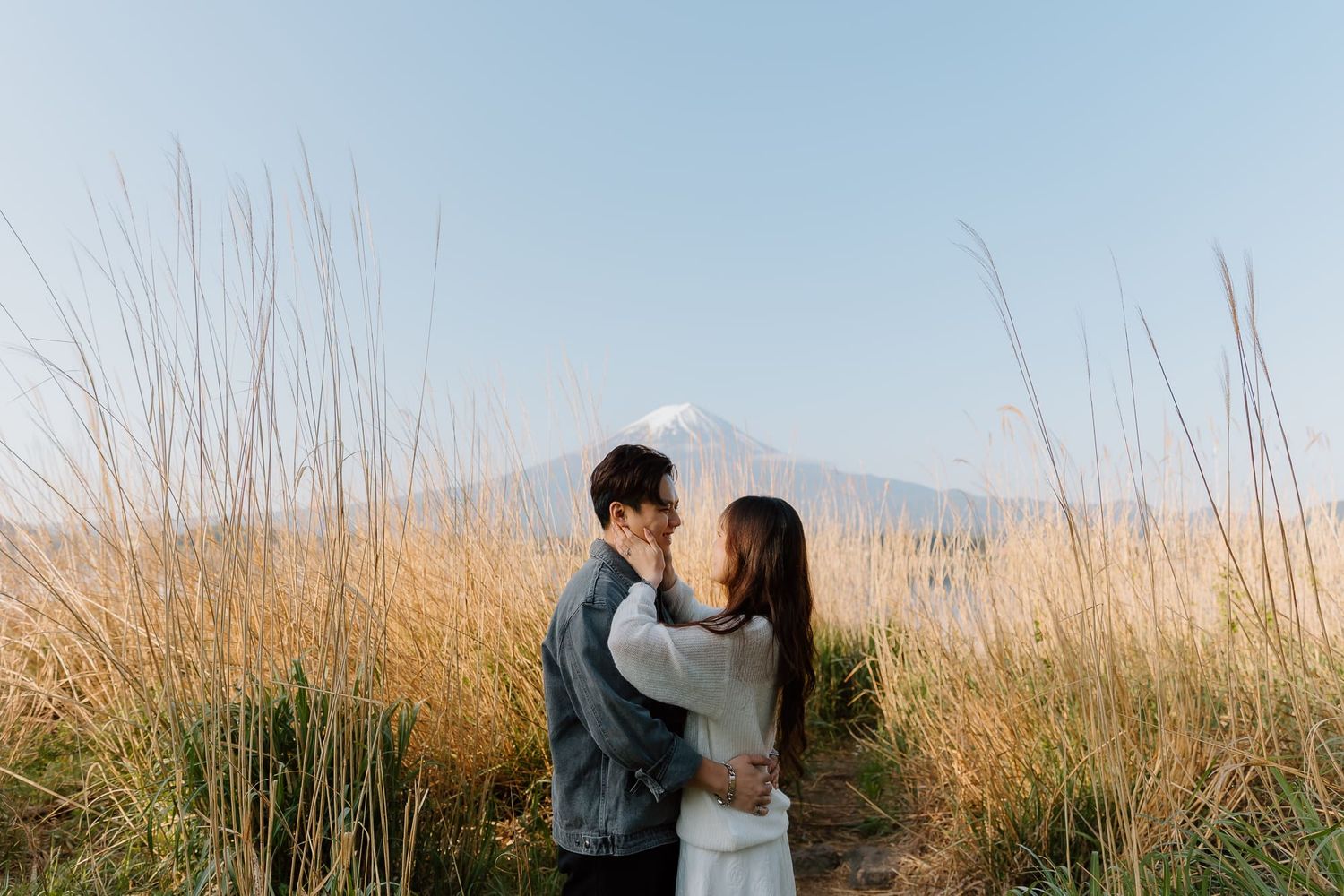 Couple embracing in golden grass field with Mount Fuji in background on a clear day.