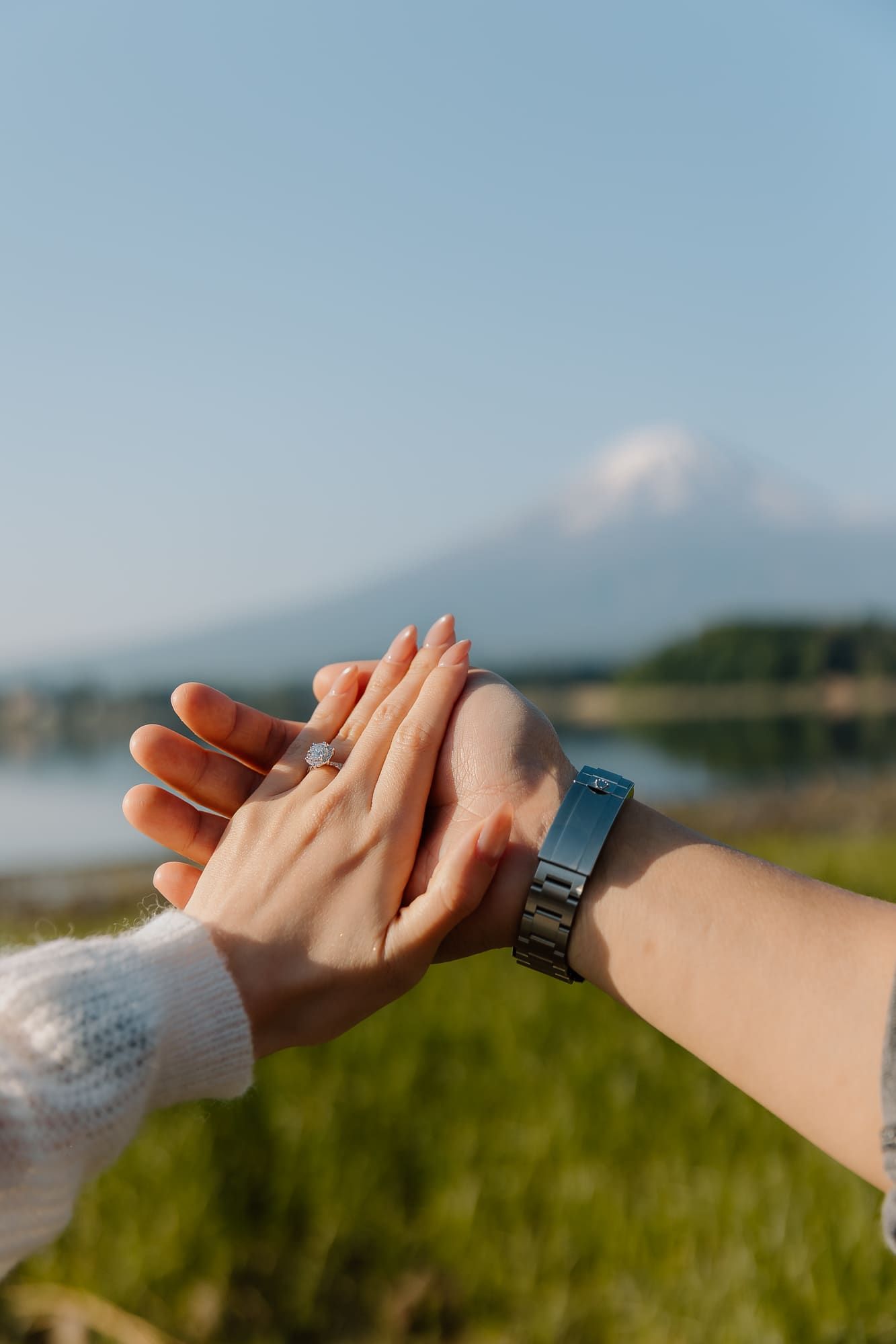 Two hands touching with a ring, black watch, and Mount Fuji in the background on a clear day.