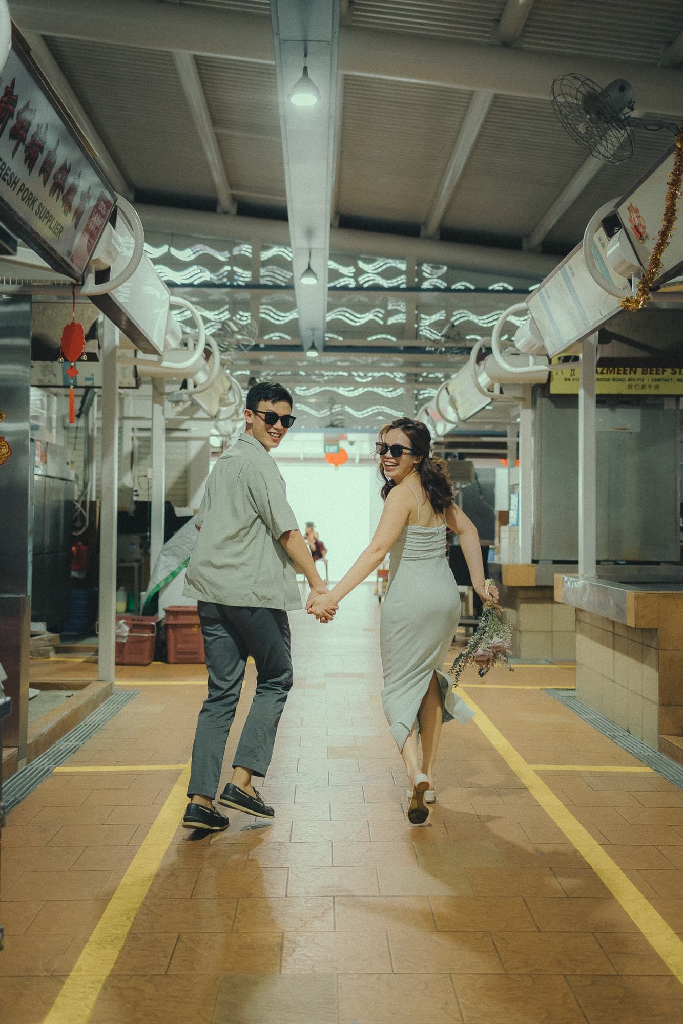A couple holding hands and running playfully through a covered walkway with decorative lattice ceiling.
