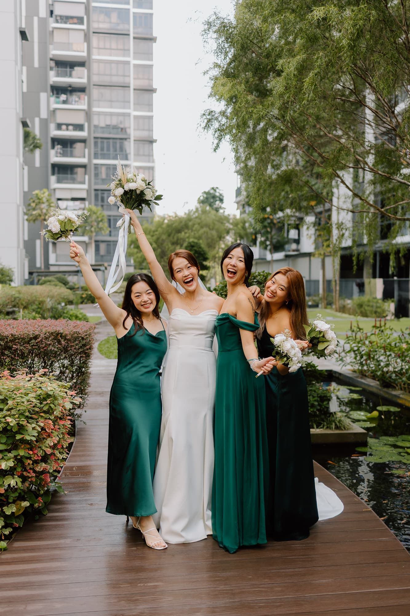 Wedding party in emerald green dresses celebrating on wooden deck with landscaped garden.
