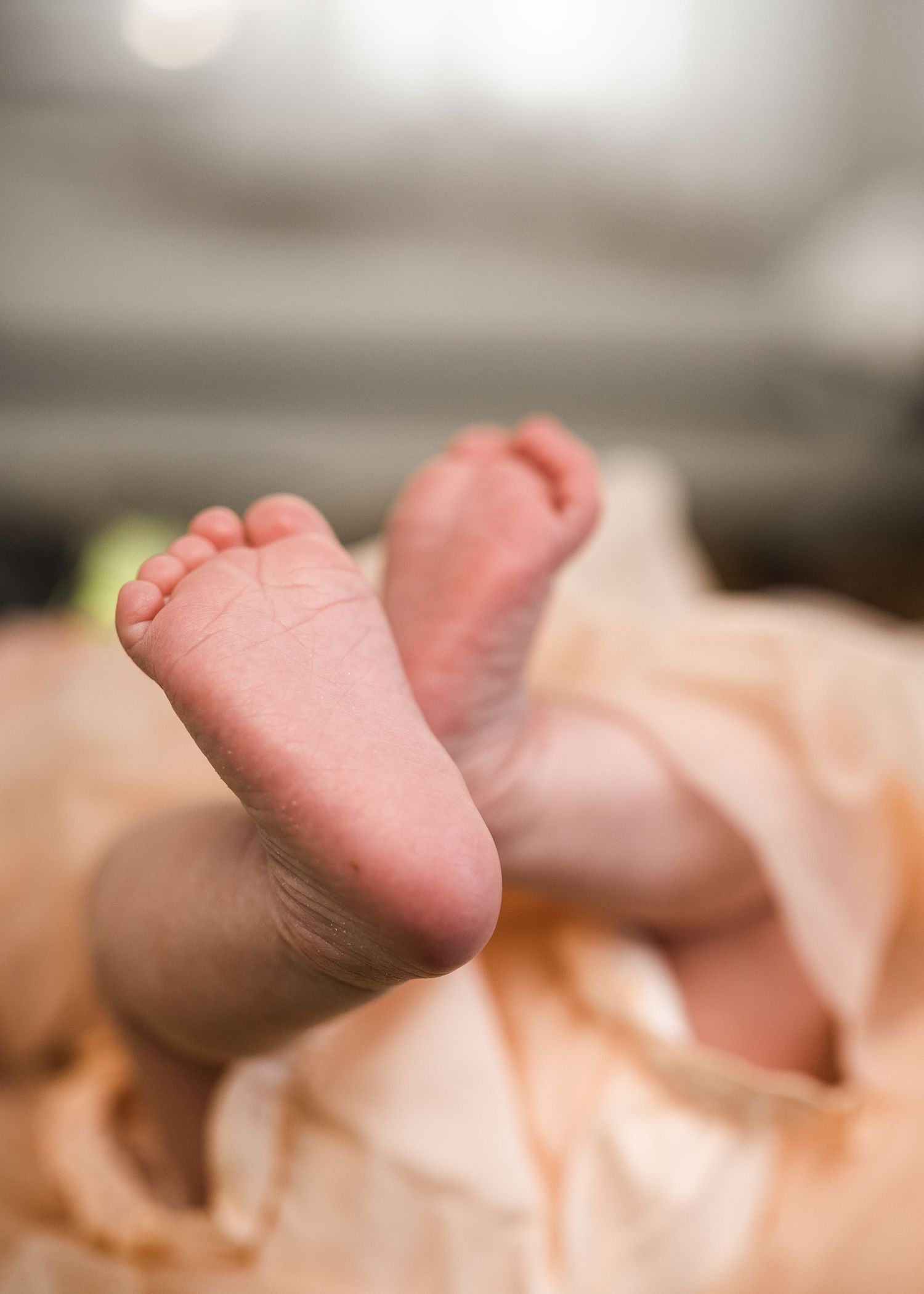 Tiny newborn baby feet wrapped in soft peachy fabric showing delicate toes.