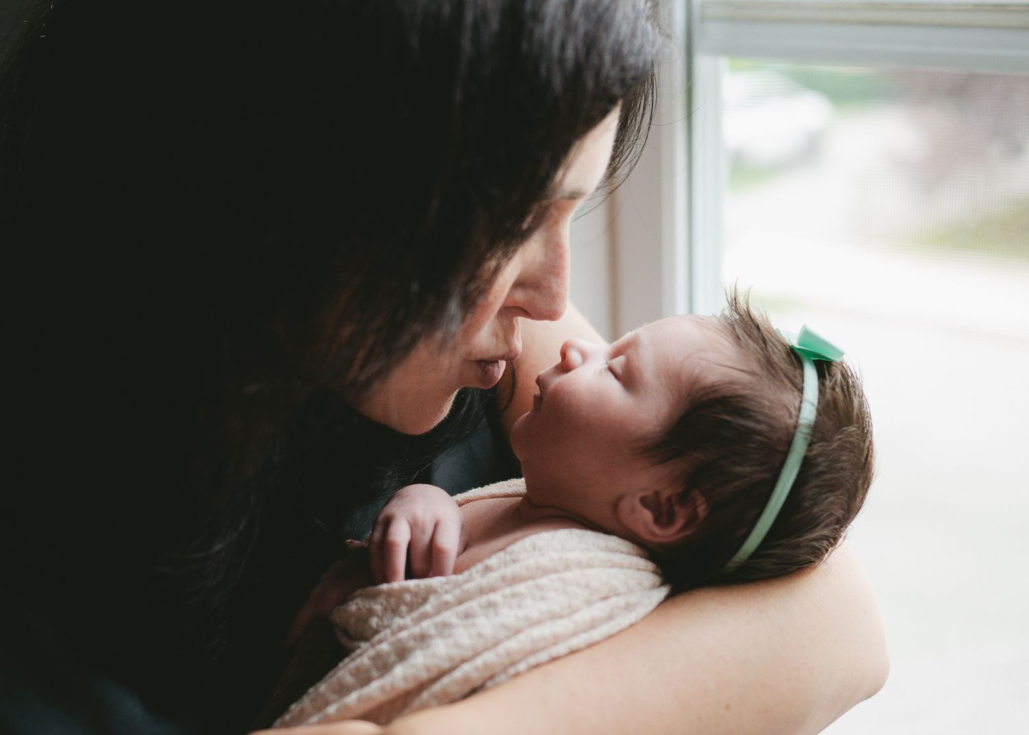 Tender moment captured between caregiver and baby by window light.