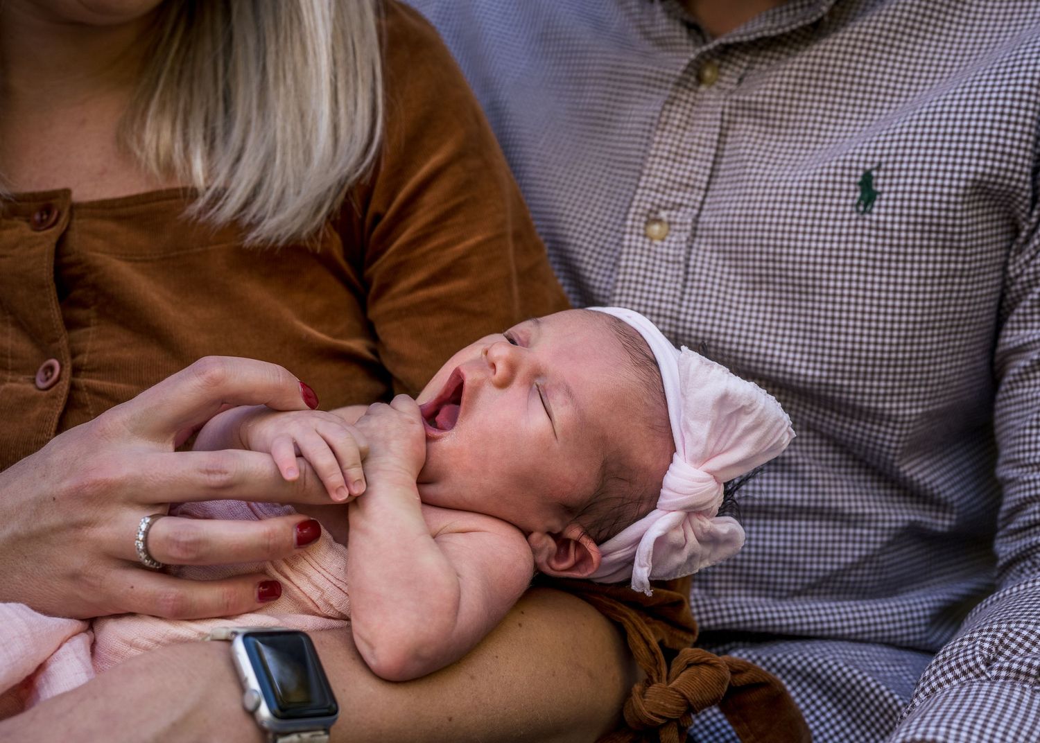 Closeup of sleepy newborn baby being cradled by parents.