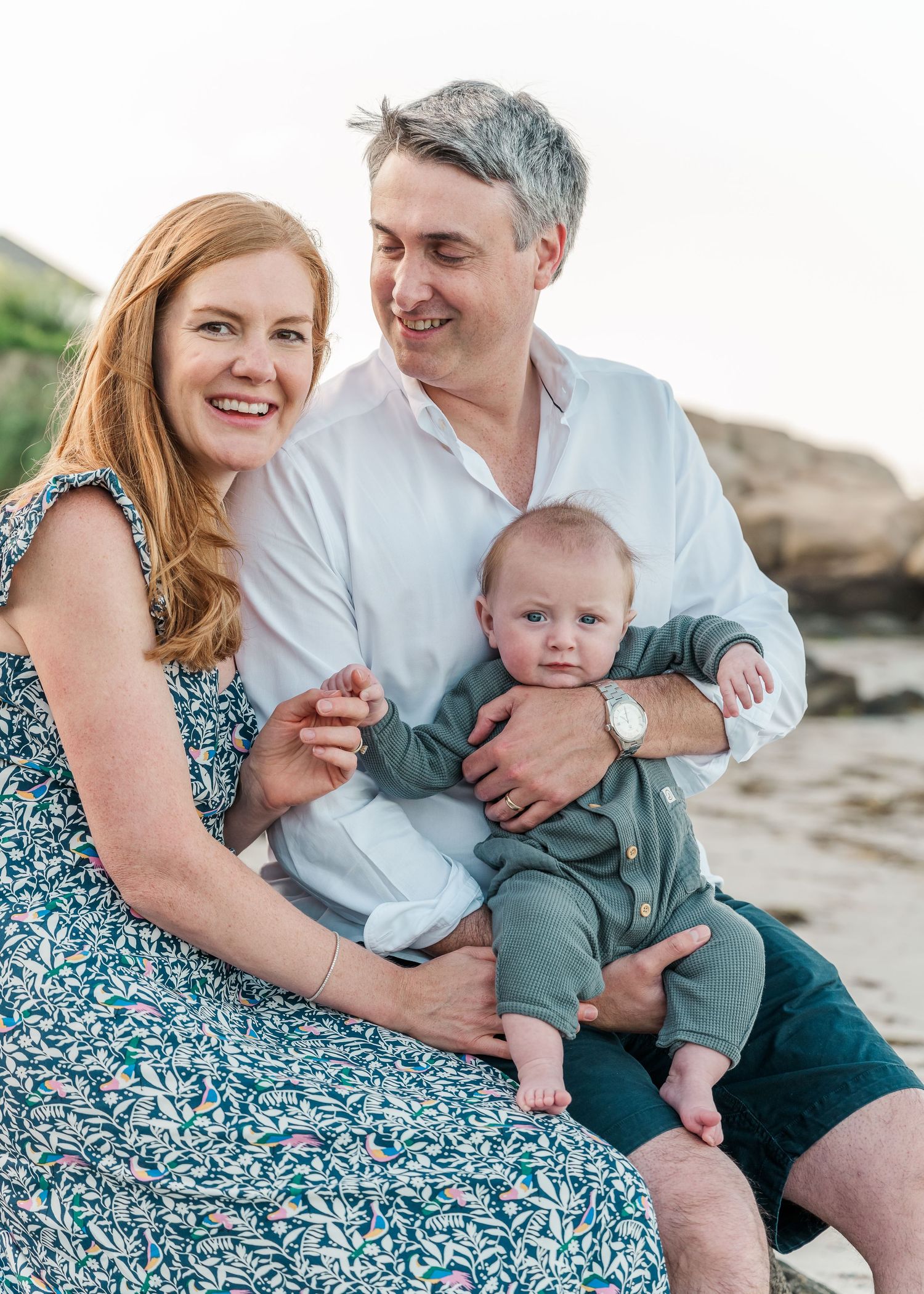 A loving family portrait taken at the beach with rocky outcrops in the background.