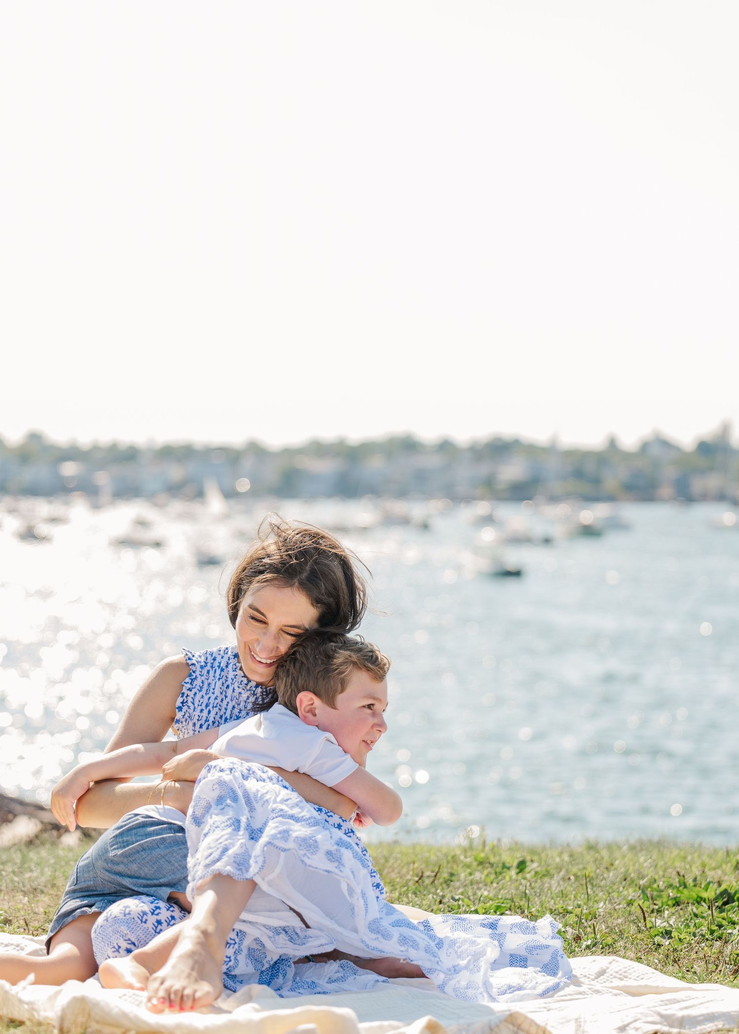 A tender moment shared between two people relaxing on grass by a serene waterfront with boats in the background.