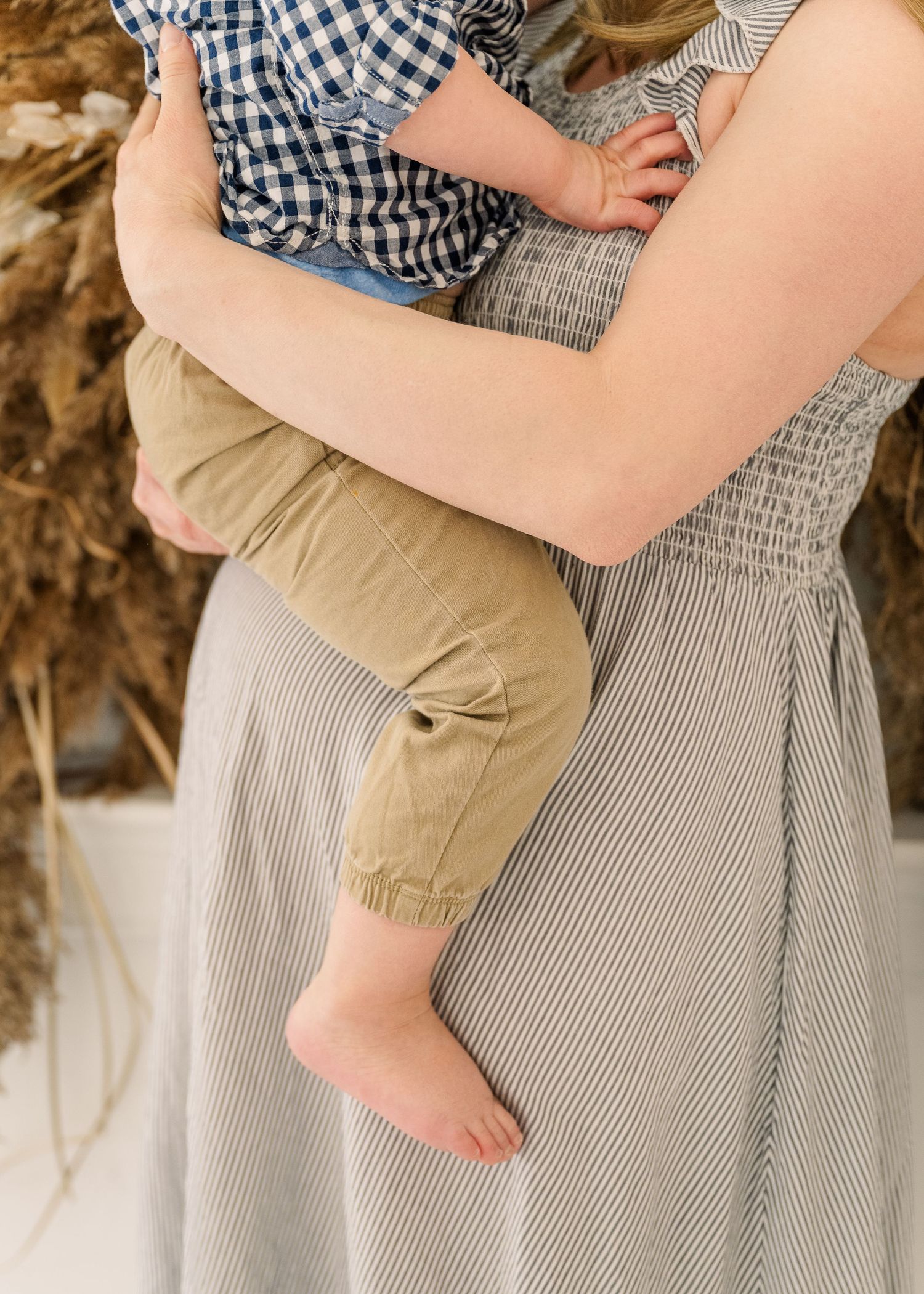 A tender moment showing bare feet and arms holding a small child wearing a gingham shirt against a gray dress.
