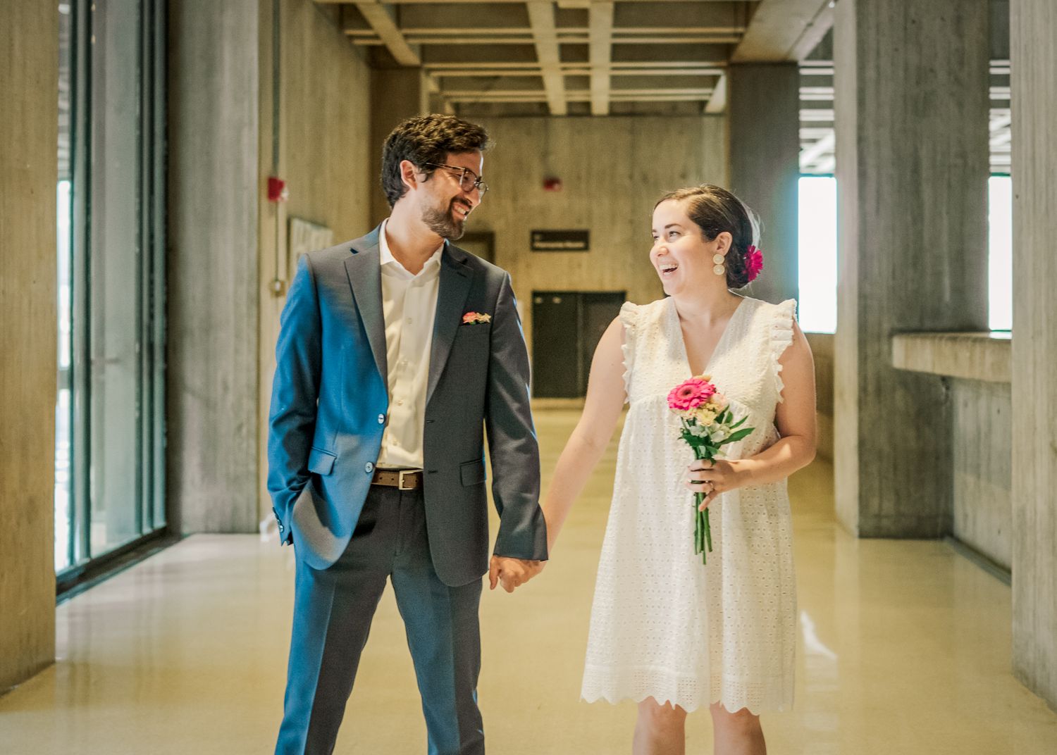 Newlyweds share a lighthearted moment in a modern building interior.