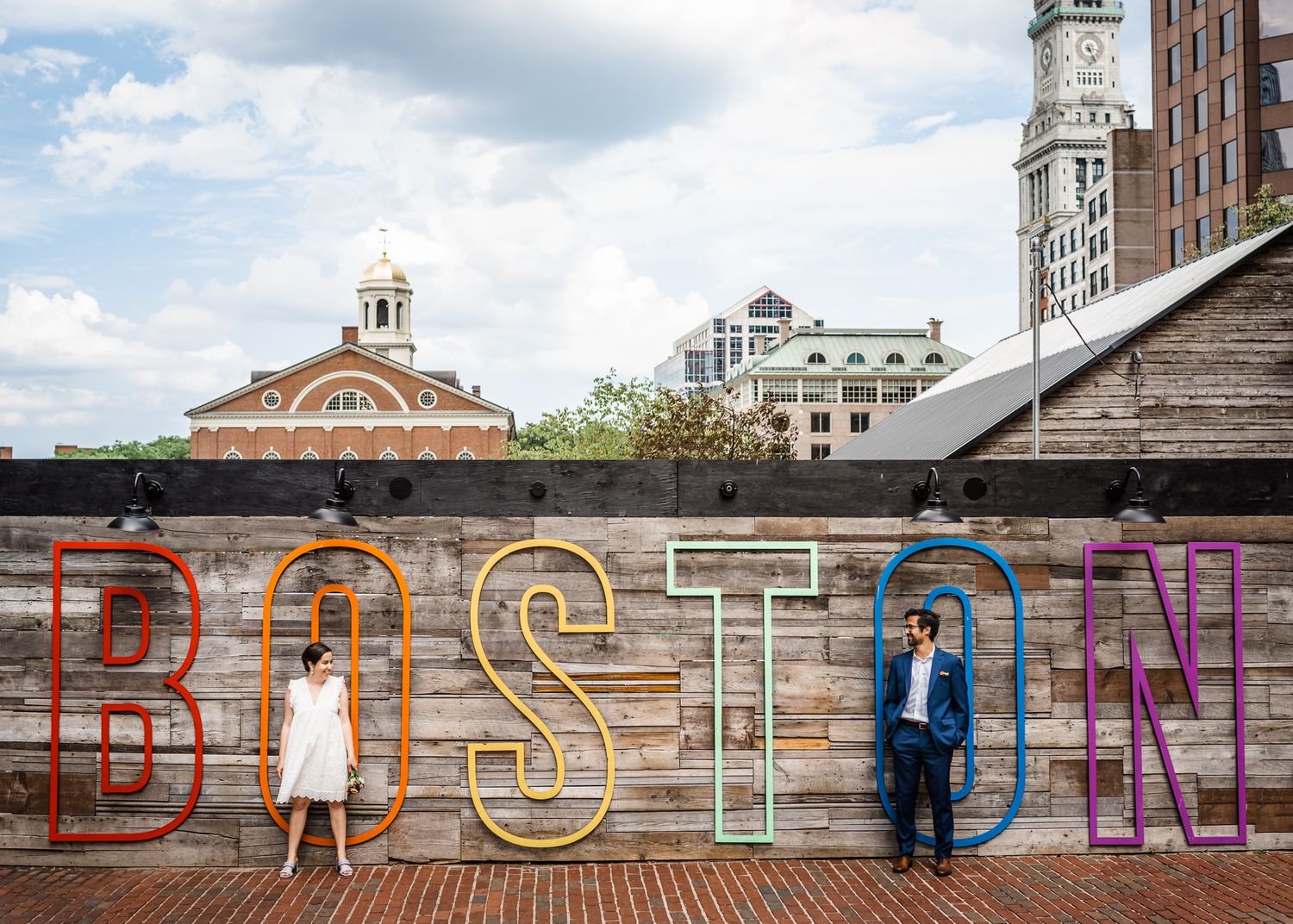 Urban rooftop photo with couple standing against vintage 'BOSTON' signage.