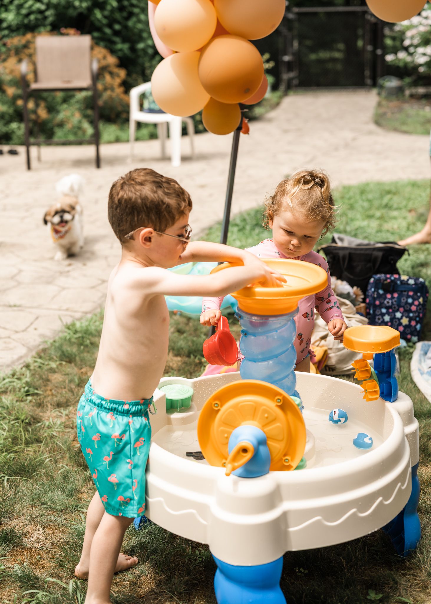 Children playing at an outdoor water table with orange balloons and toys.