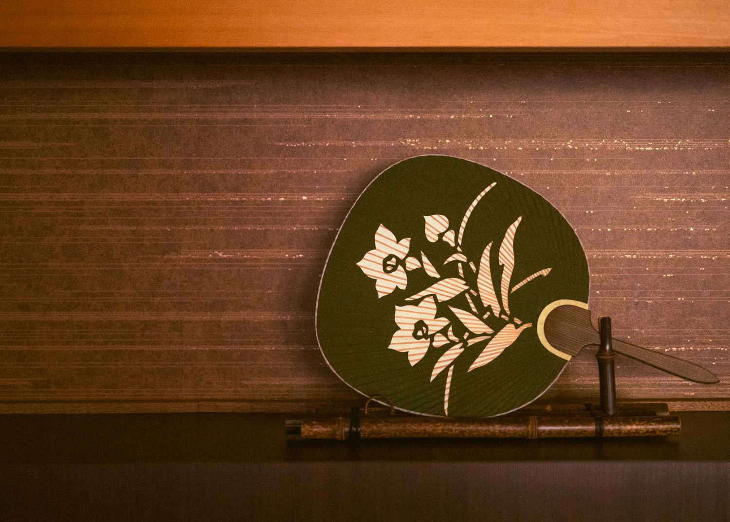 Decorative round green plate with white floral design displayed on wooden shelf.