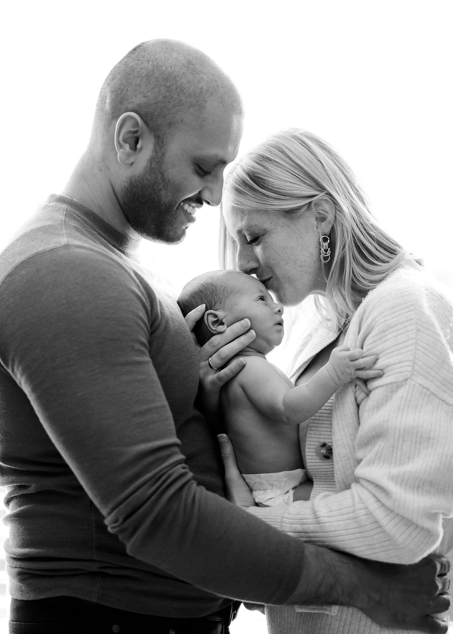 A tender black and white family portrait showing intimate bonding moment with a newborn baby.