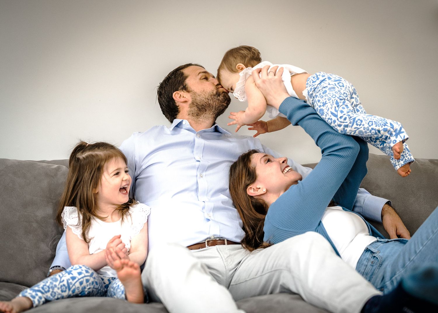 A playful family moment on a gray couch showing affection and laughter.