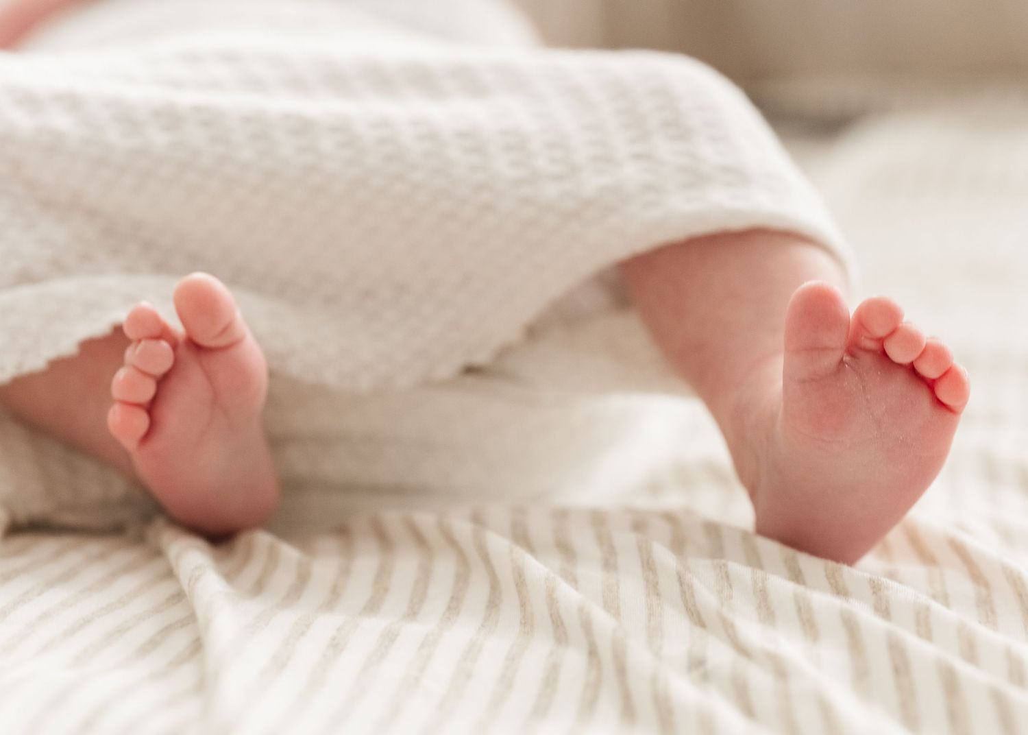 Tiny newborn baby feet peeking out from under a soft white knitted blanket.